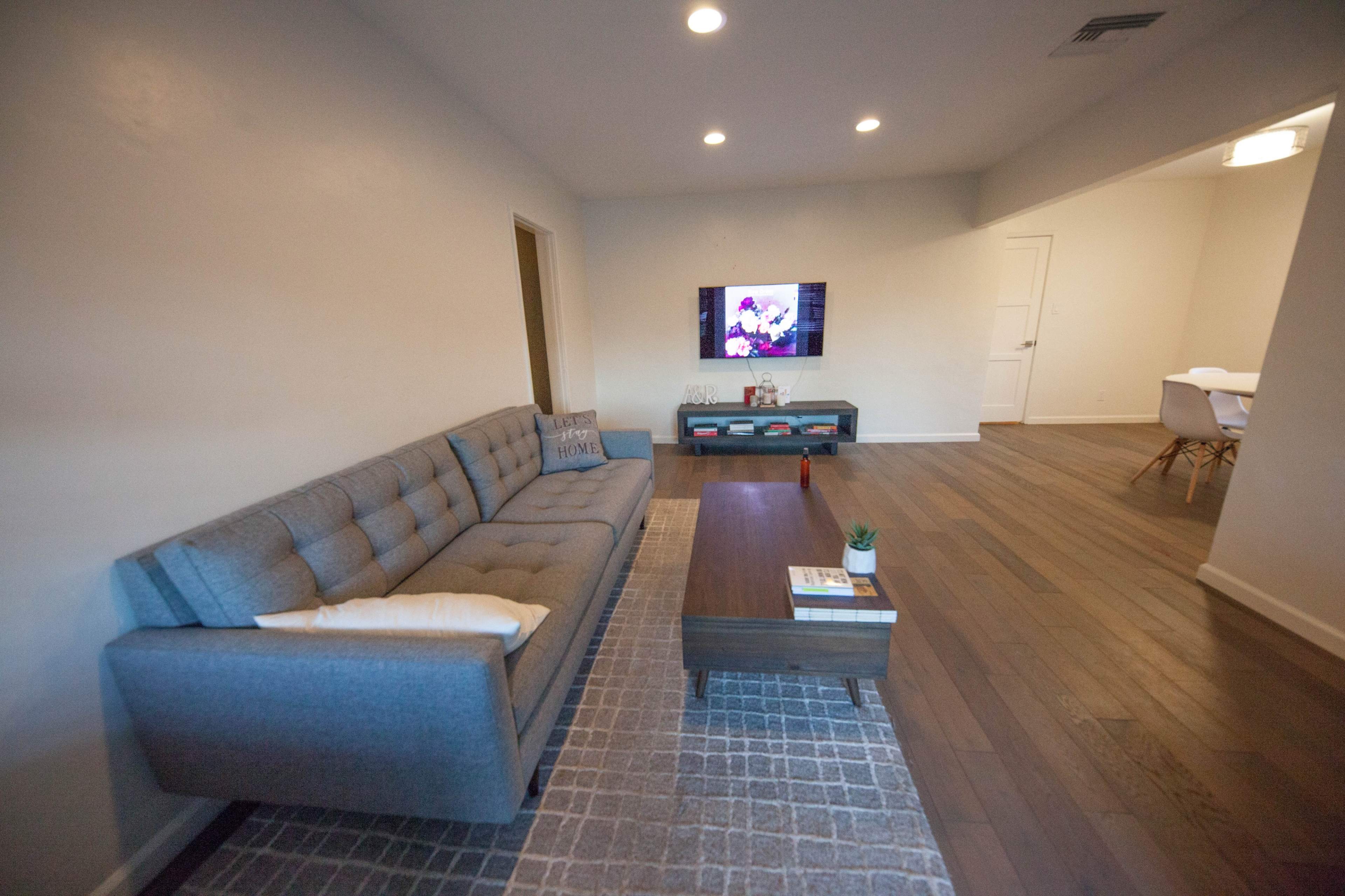 A living room with a gray sofa, a coffee table, a TV mounted on the wall, and hardwood flooring.