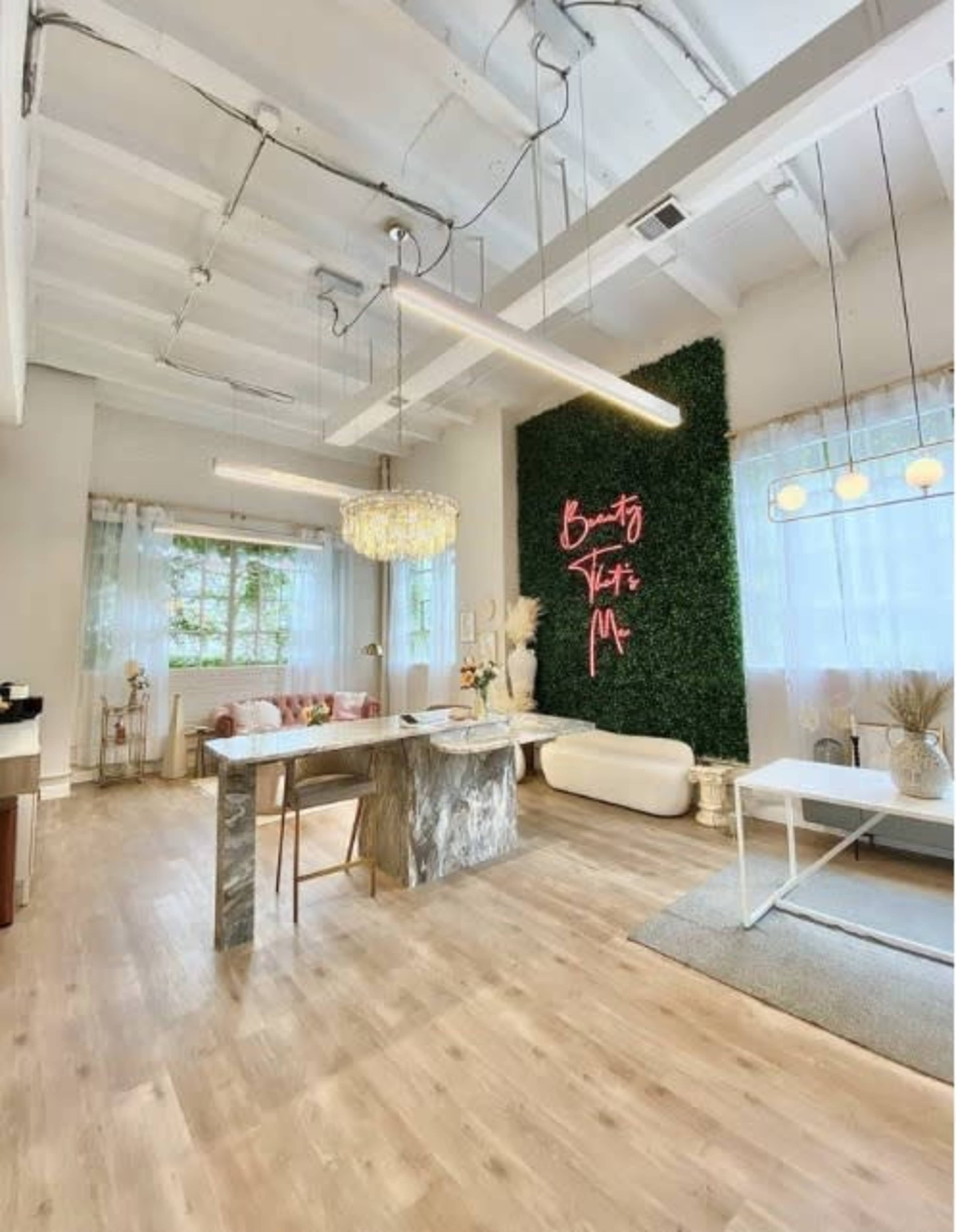 The image shows a modern interior space featuring a green wall with neon signage, a chandelier, and a mix of contemporary furniture.