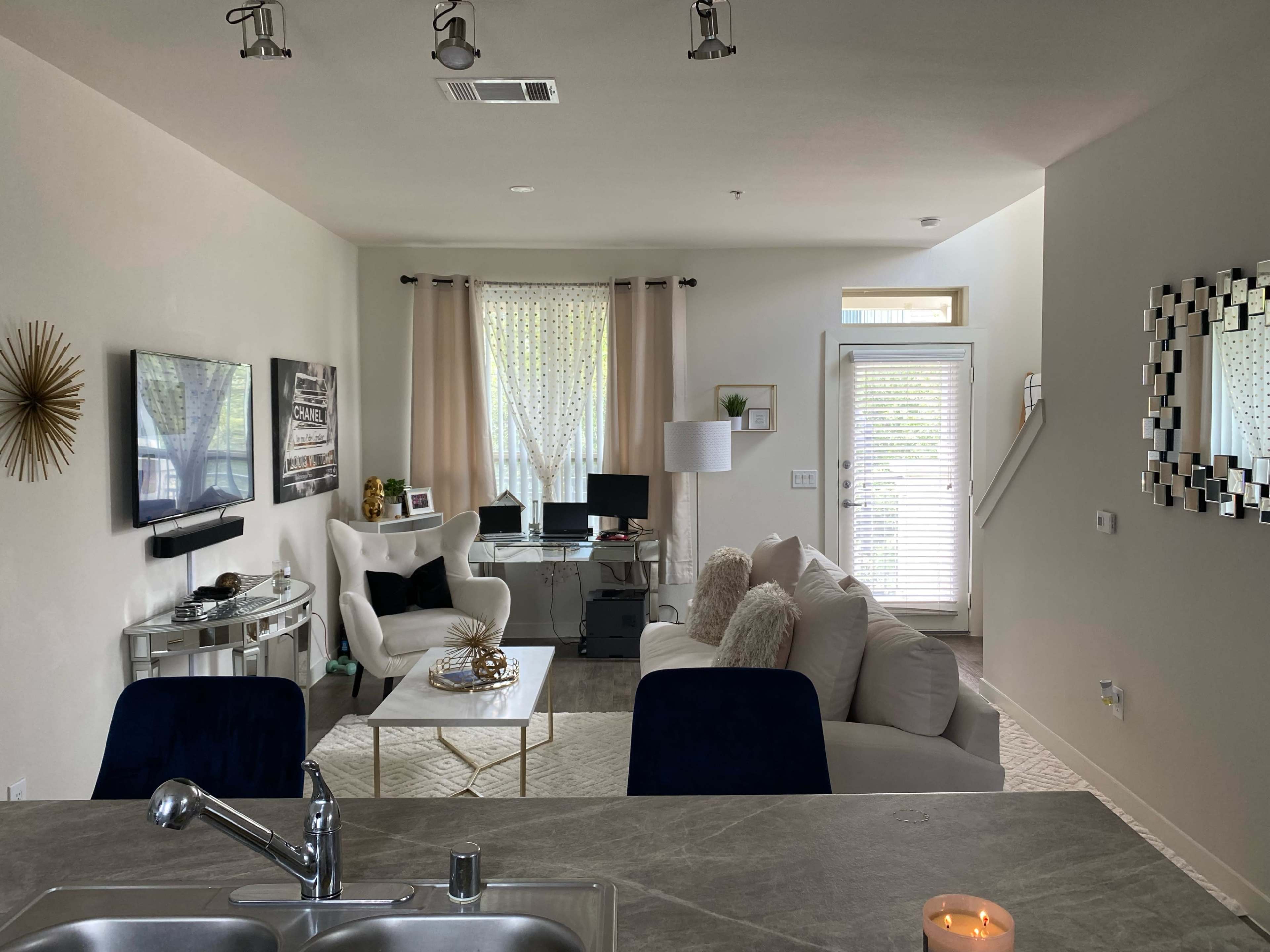 The image shows a modern living room with a white couch, a coffee table, a TV area, and a small workspace near a window.