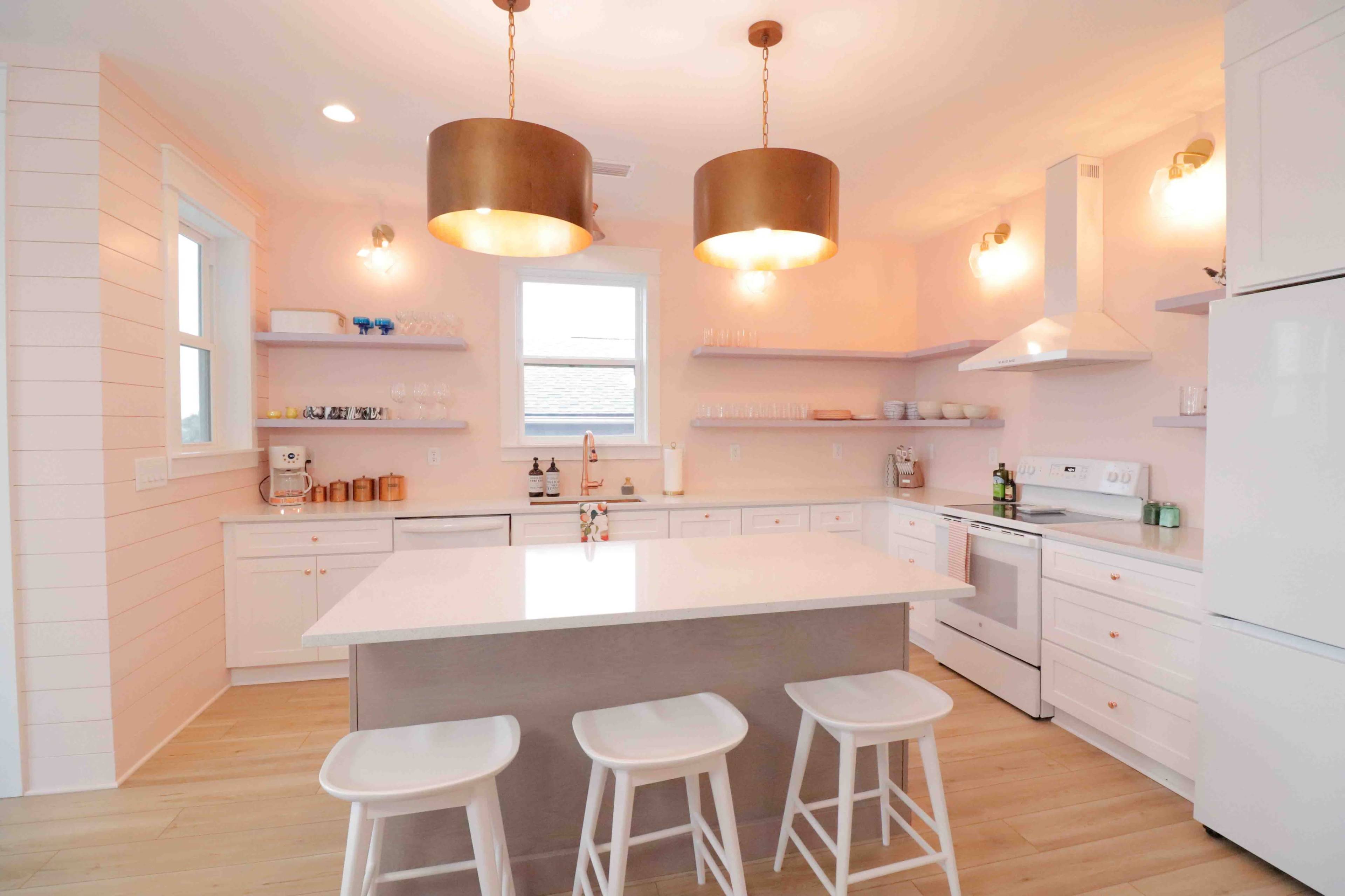 A modern kitchen with white cabinetry, a central island with seating, and pendant lights above.