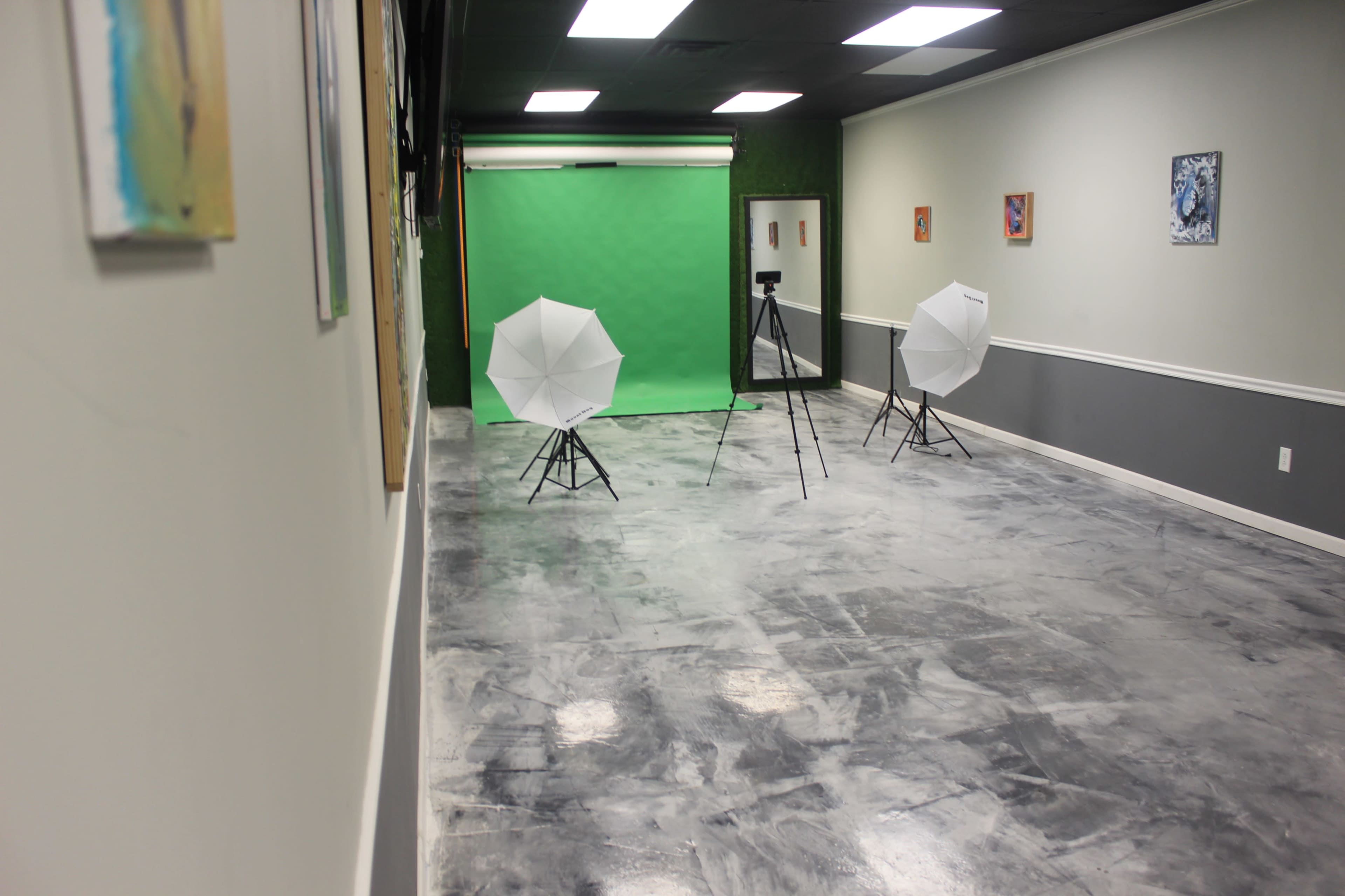 The image shows a photography studio with a green backdrop, two softbox lights on tripods, and a concrete floor.