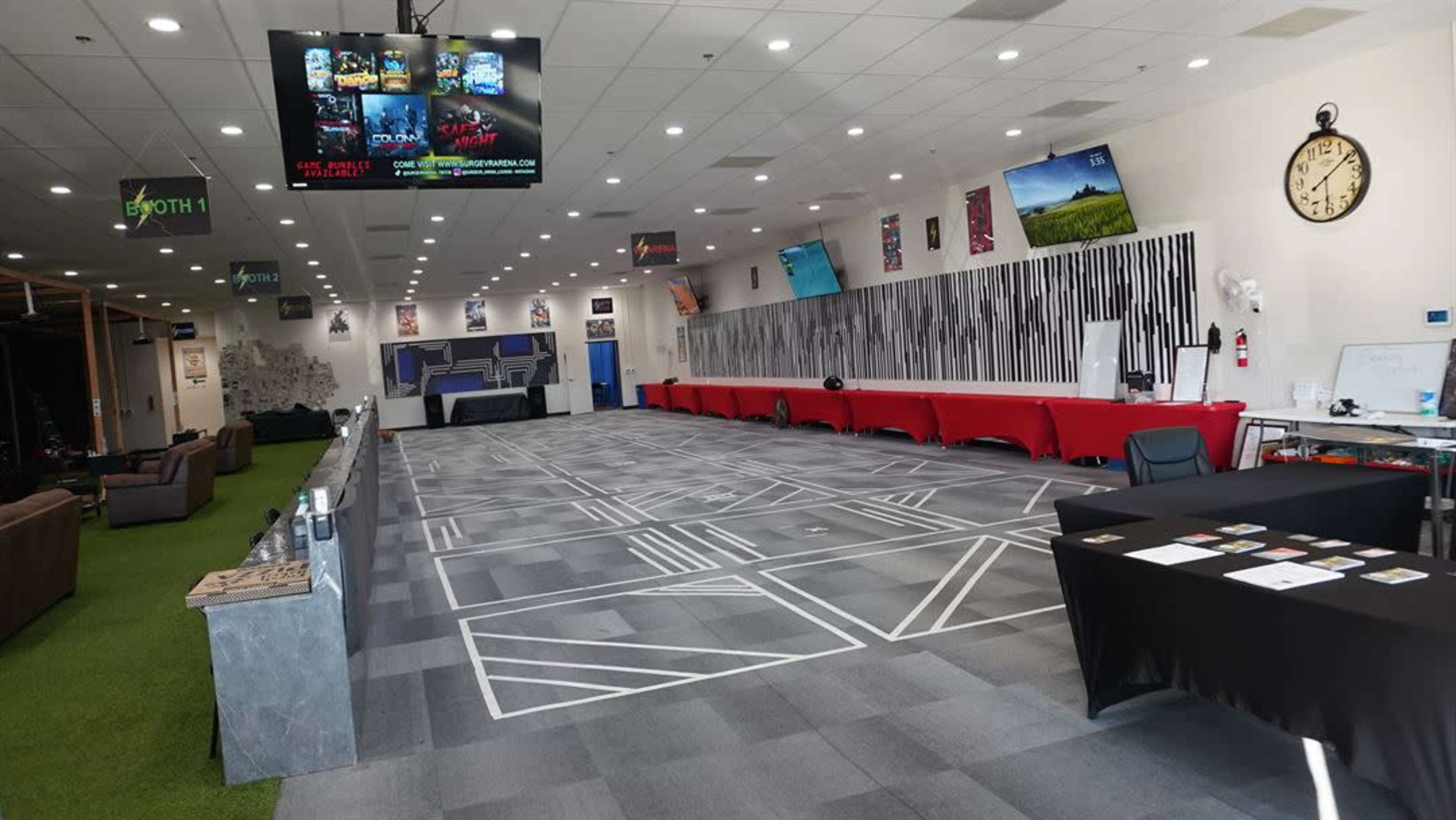 The image shows a spacious, well-lit indoor area with a patterned carpet, rows of tables covered in red and black cloths, and multiple screens displaying various images and information.