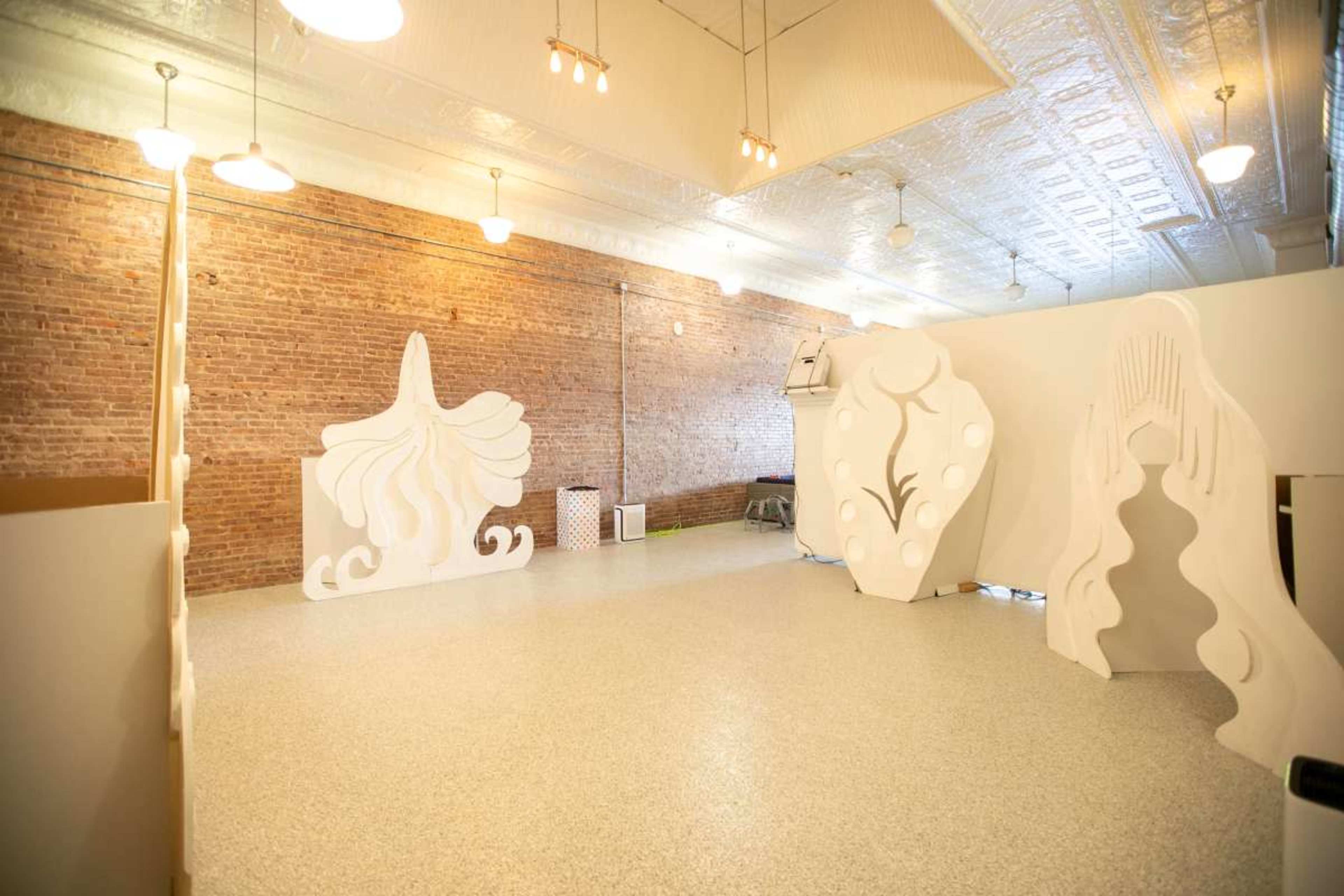 The image shows an interior space with textured brick walls and several large, abstract white sculptures arranged across the floor.