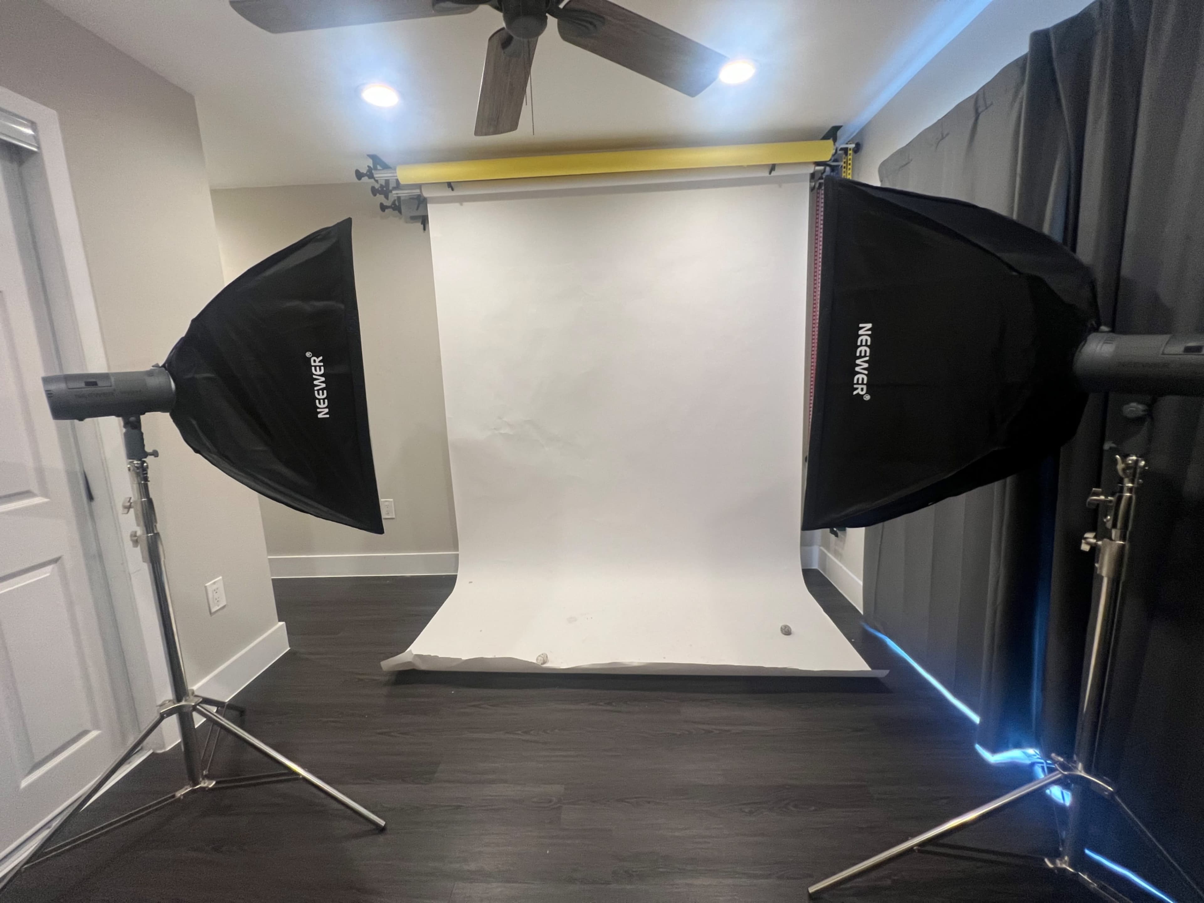 A photography studio setup with two softbox lights positioned on either side of a white backdrop.