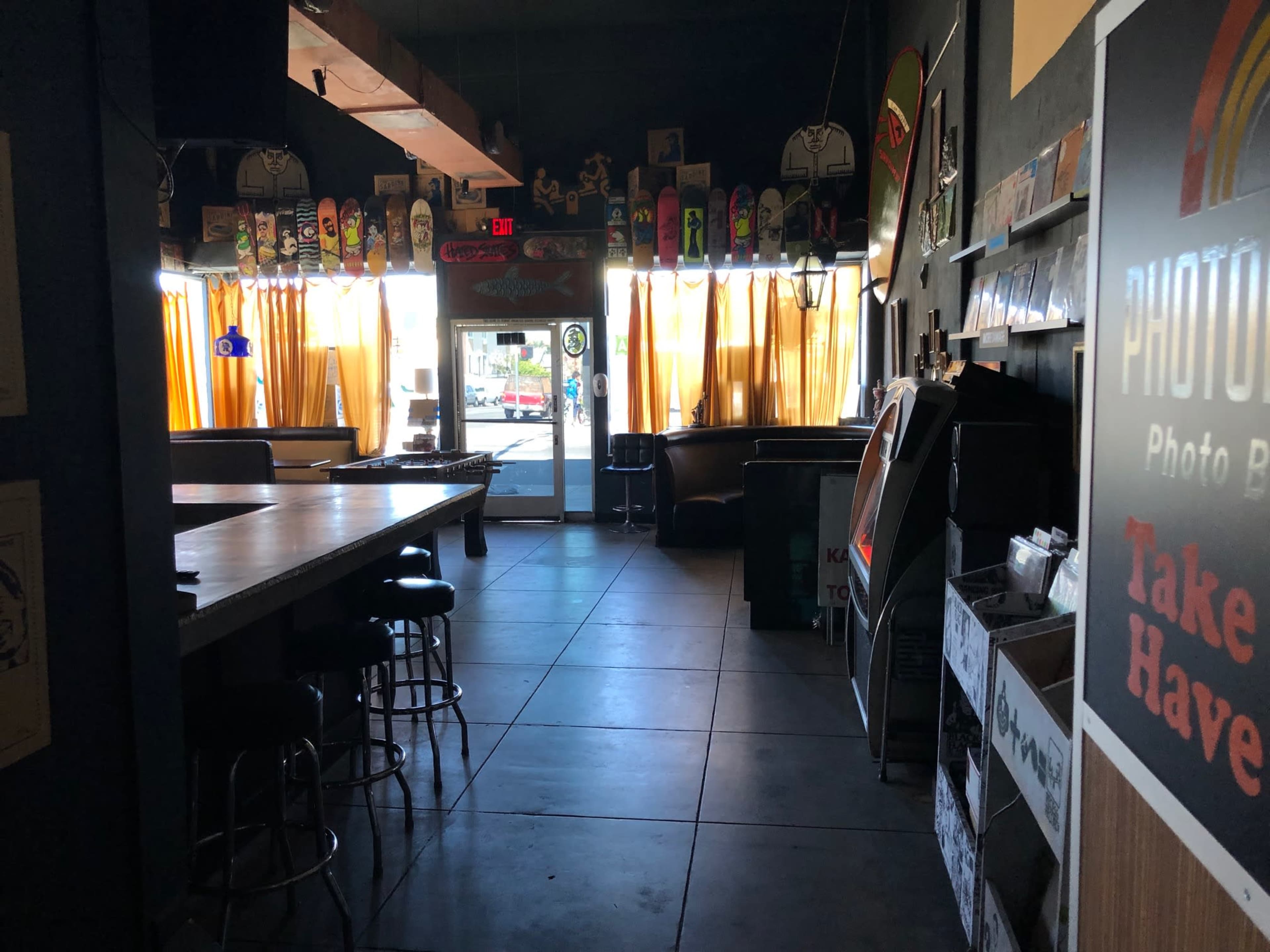 An interior of a cafe or bar with a counter, seating areas, and large windows covered by yellow curtains.