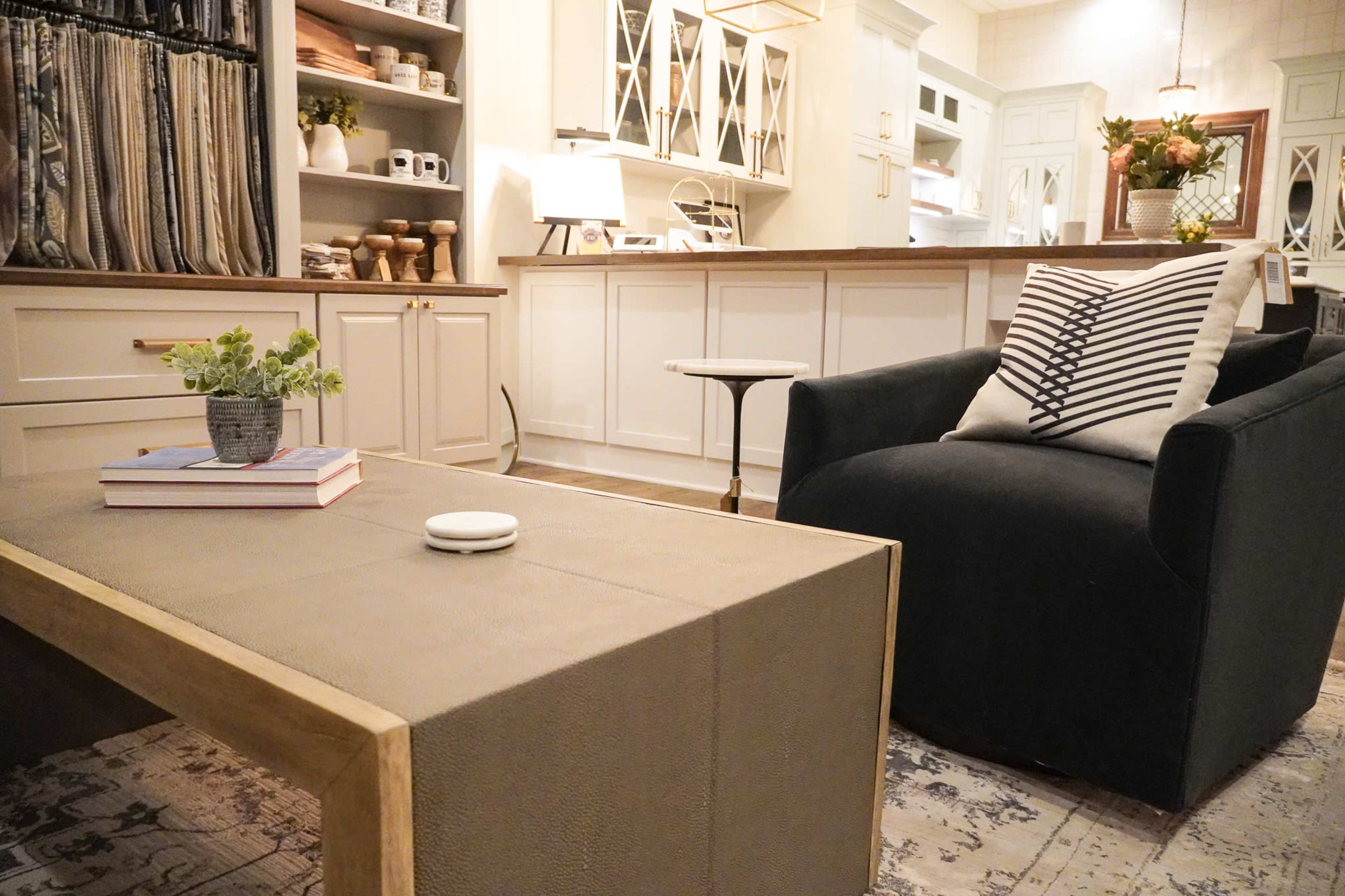 A modern living area features a black armchair, a coffee table with a textured surface, and a backdrop of neatly arranged kitchen cabinetry.