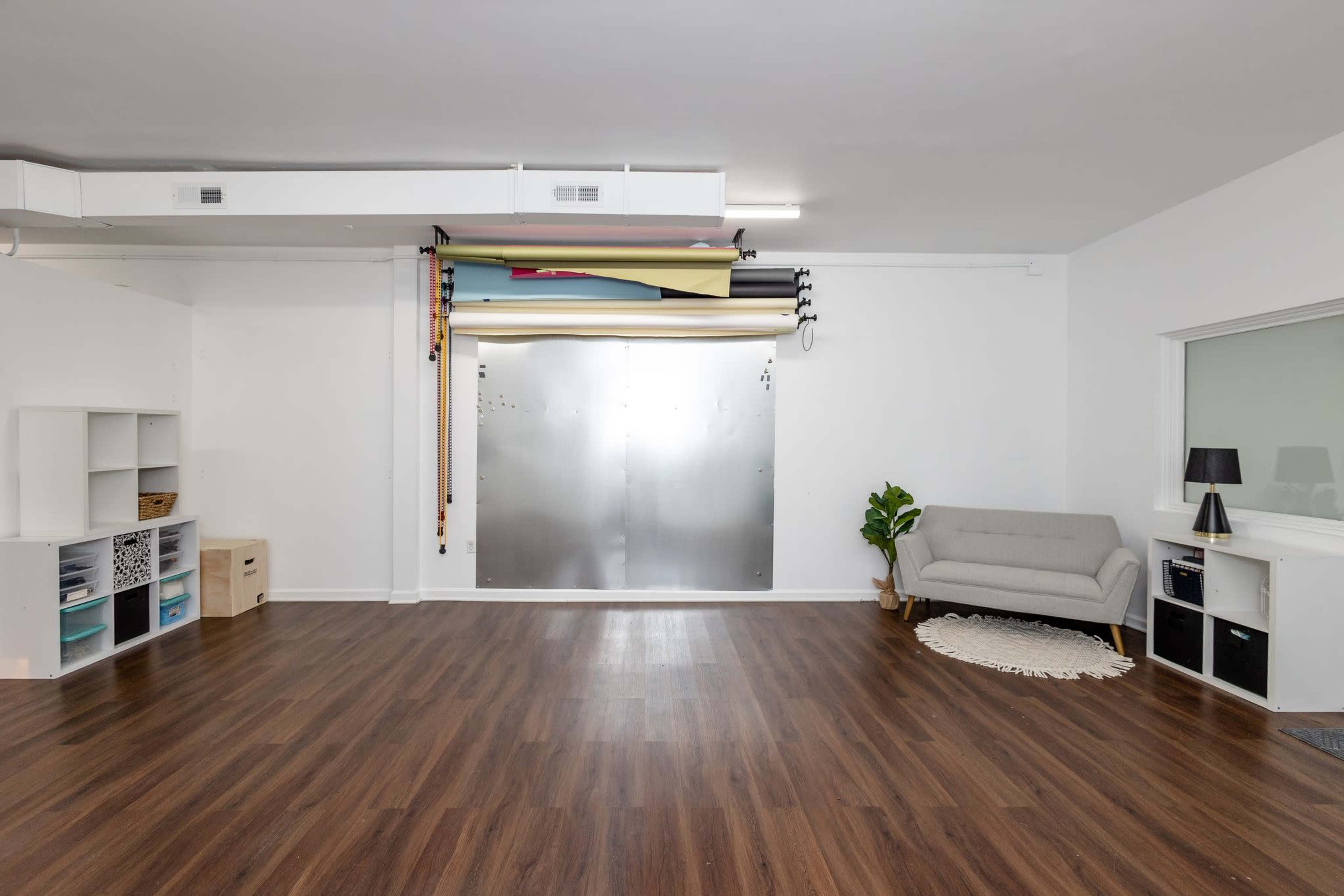 An empty studio space with hardwood floors, a light-colored sofa, storage units, and a backdrop setup against the wall.