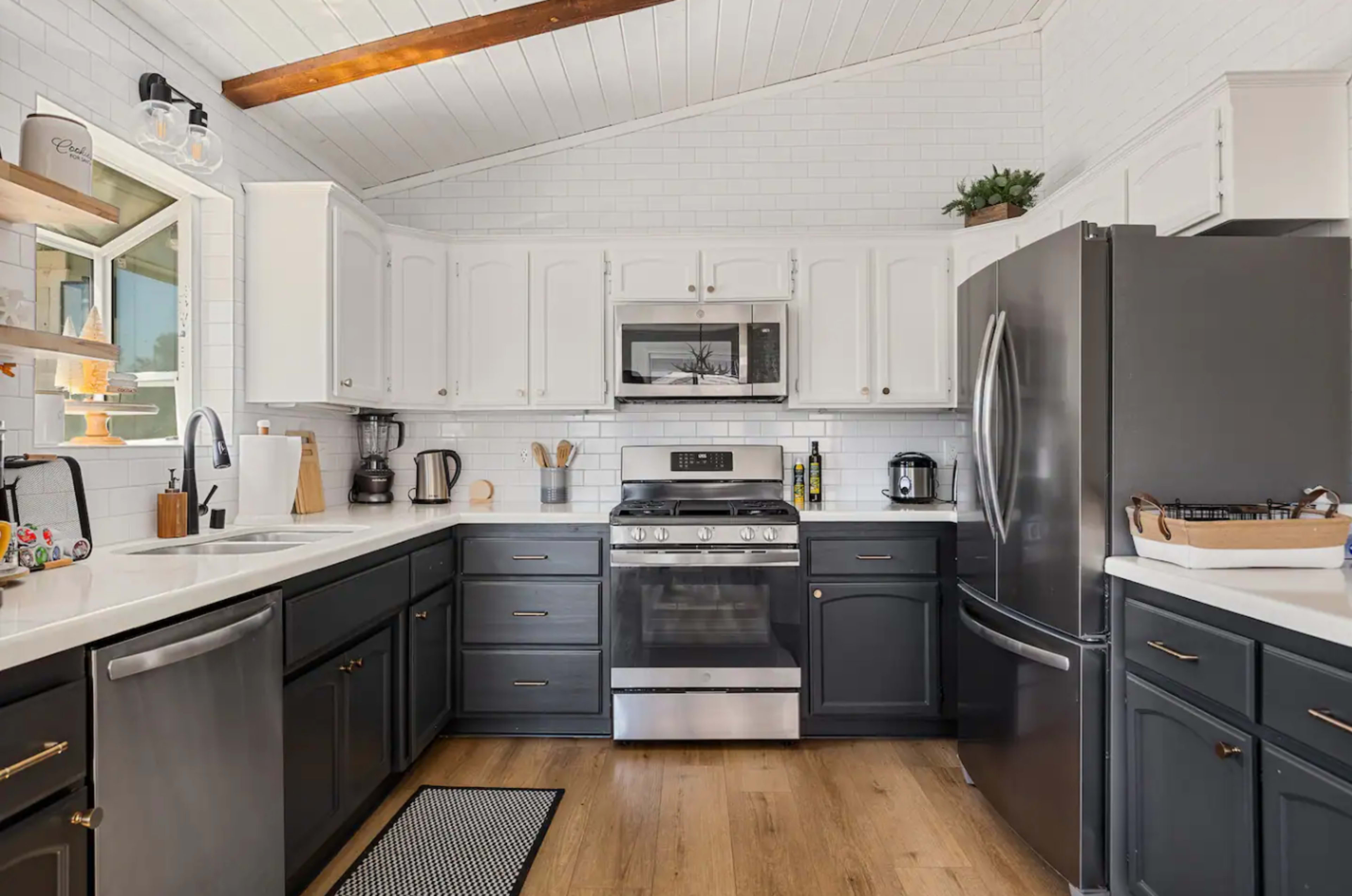 The image shows a modern kitchen with white and dark gray cabinets, stainless steel appliances, and wooden flooring.