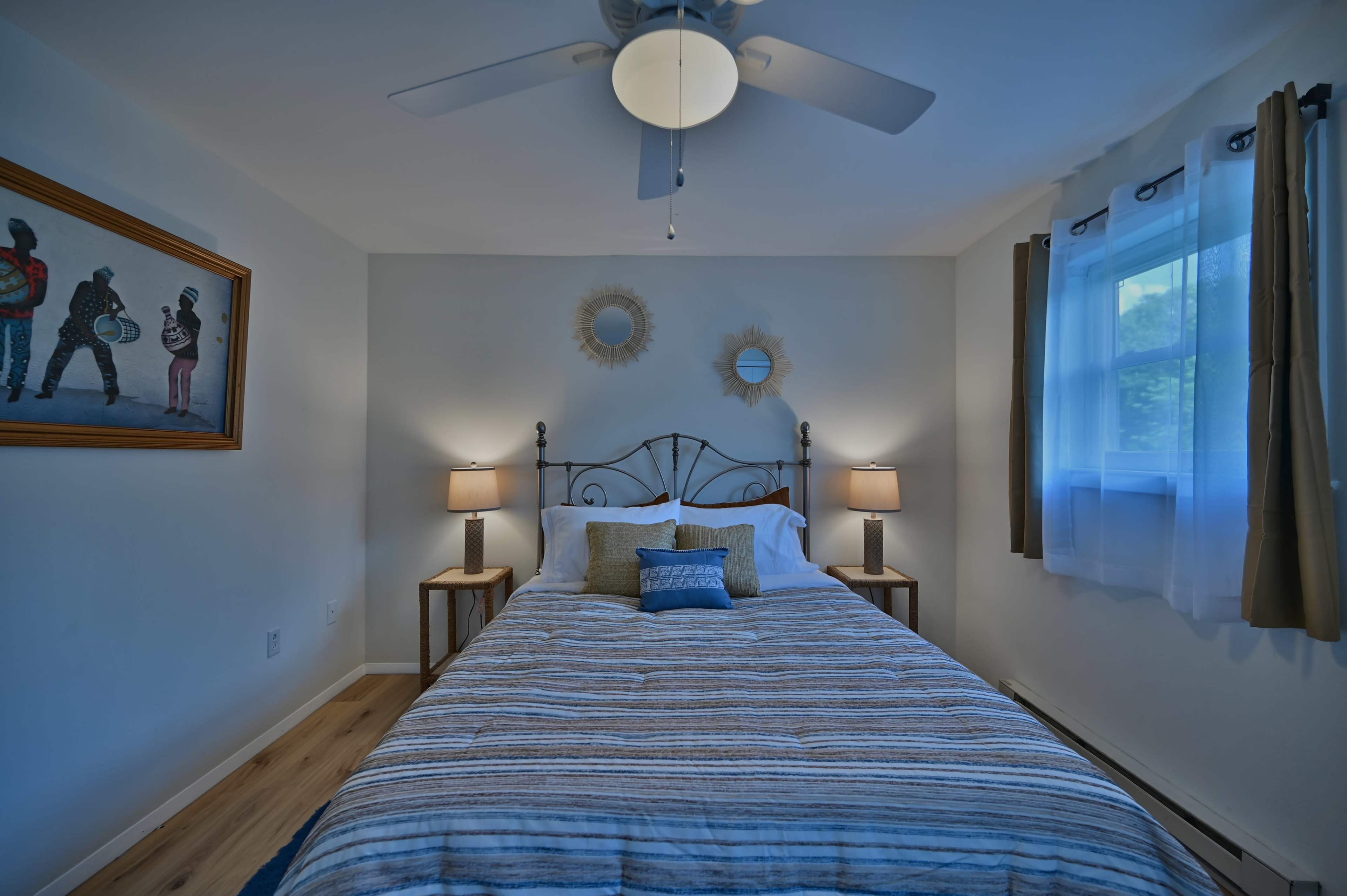 A neatly arranged bedroom with a double bed, bedside lamps, a window, and framed artwork on the wall.