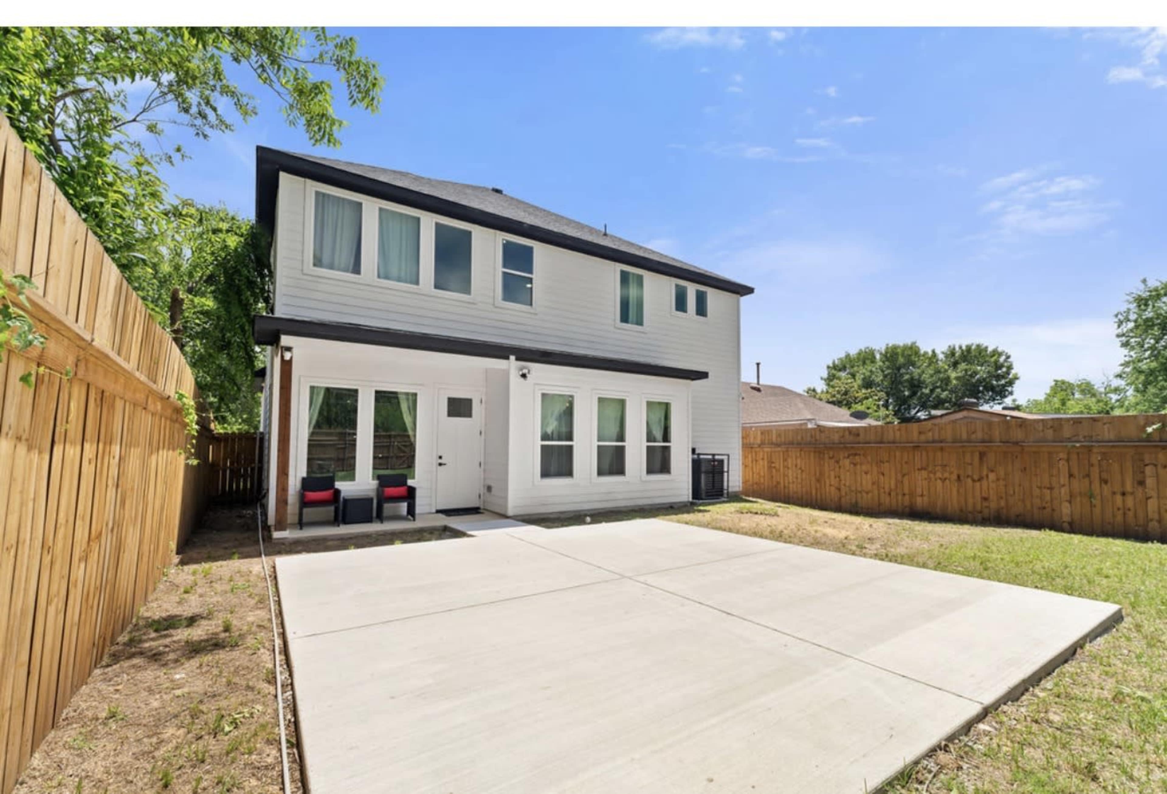 The image shows the backyard of a two-story house with a concrete patio area, surrounded by wooden fencing and grass.