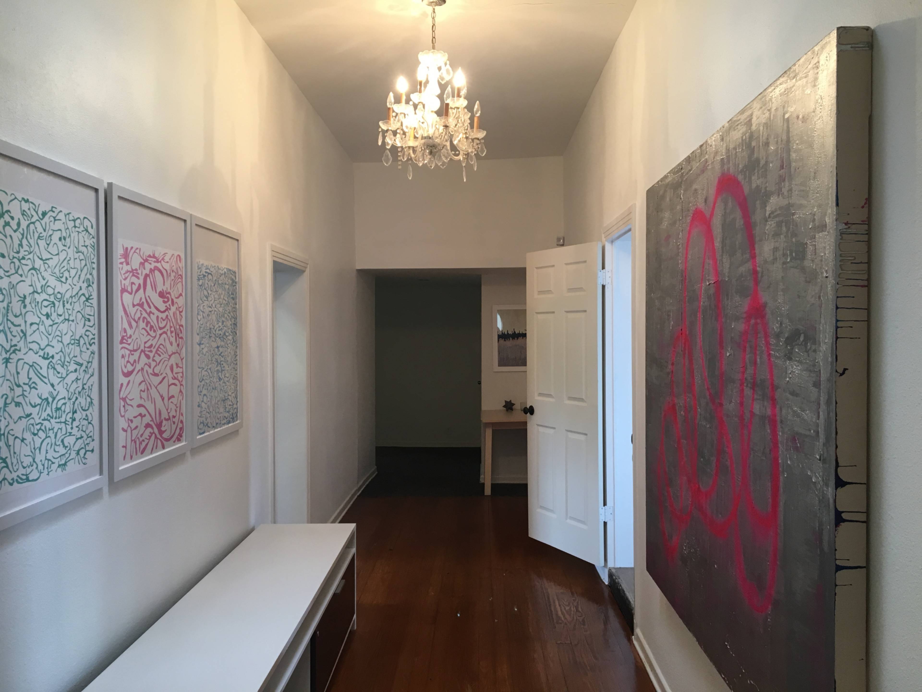 A hallway features framed artwork on the walls, a bench, and a large painting at the end, illuminated by a chandelier.