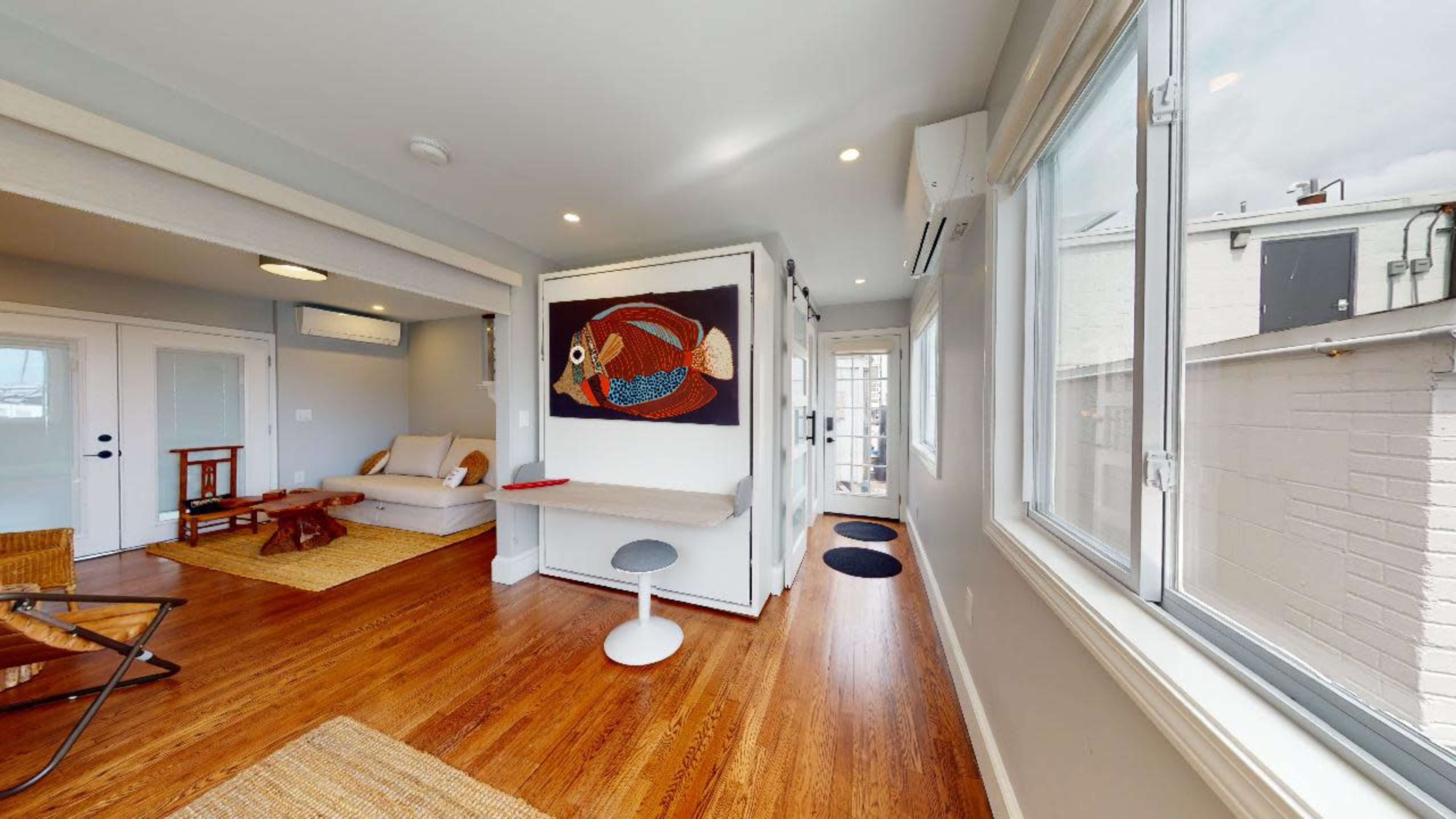 A modern living space with a sofa, a decorative wall hanging, and large windows allowing natural light.