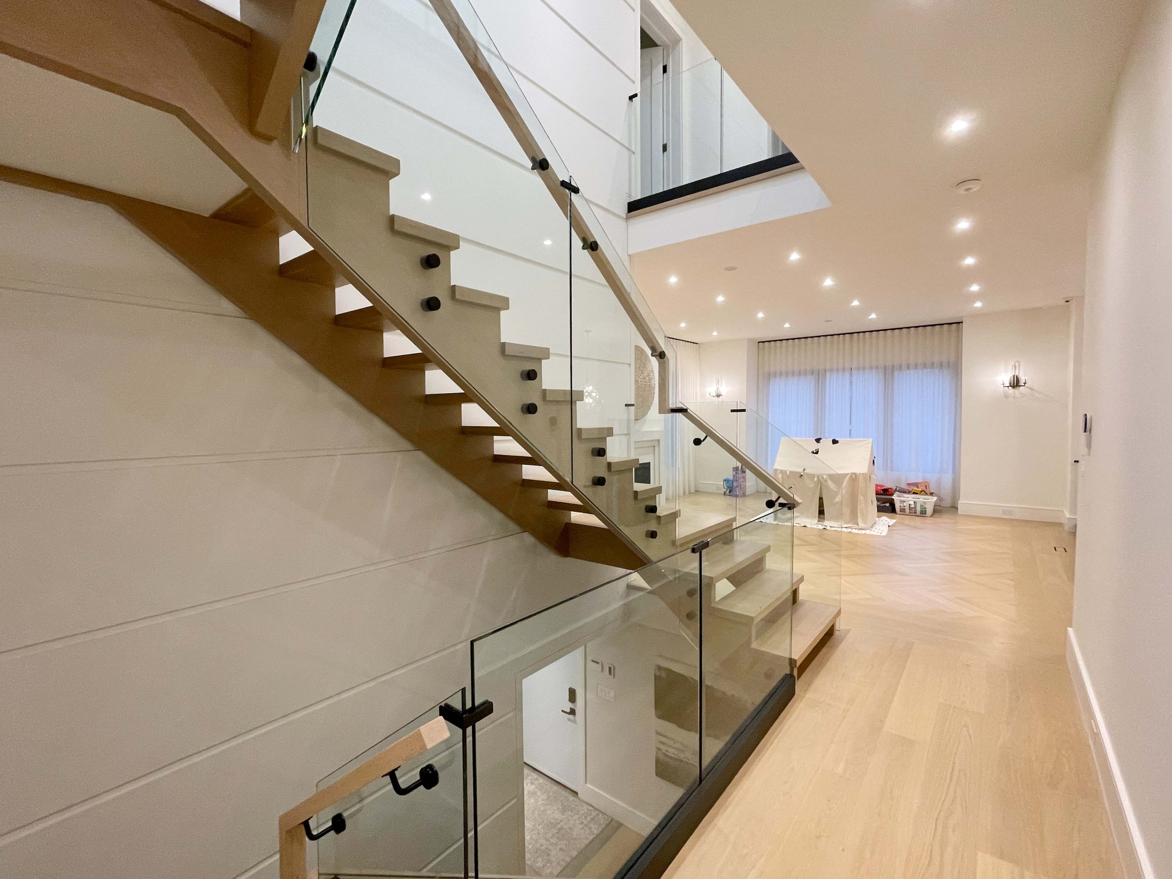 A modern interior staircase with glass railings, leading to an upper level in a well-lit entryway.