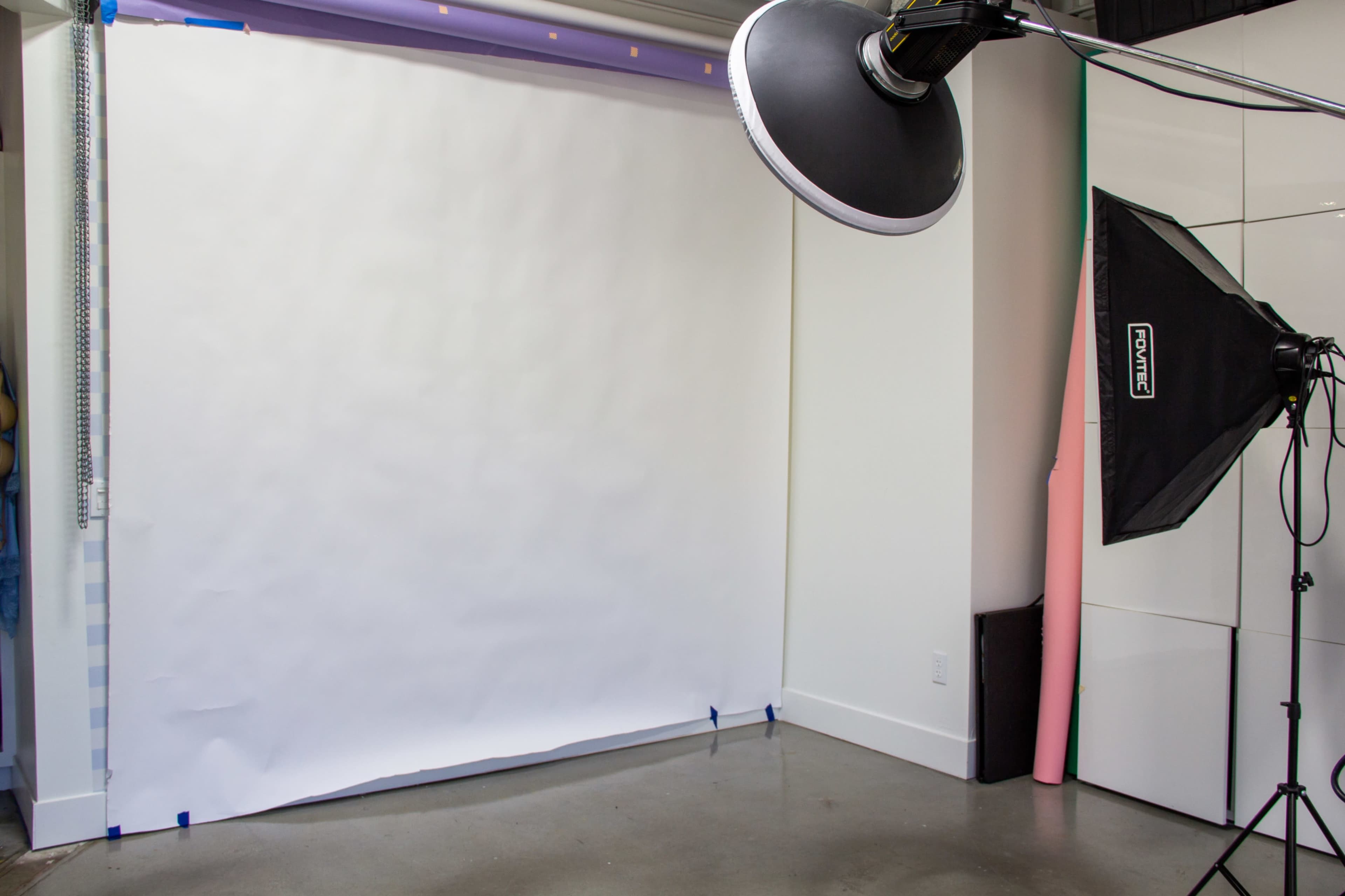 The image shows a photography studio with a white backdrop, a large lighting setup, and a smooth concrete floor.