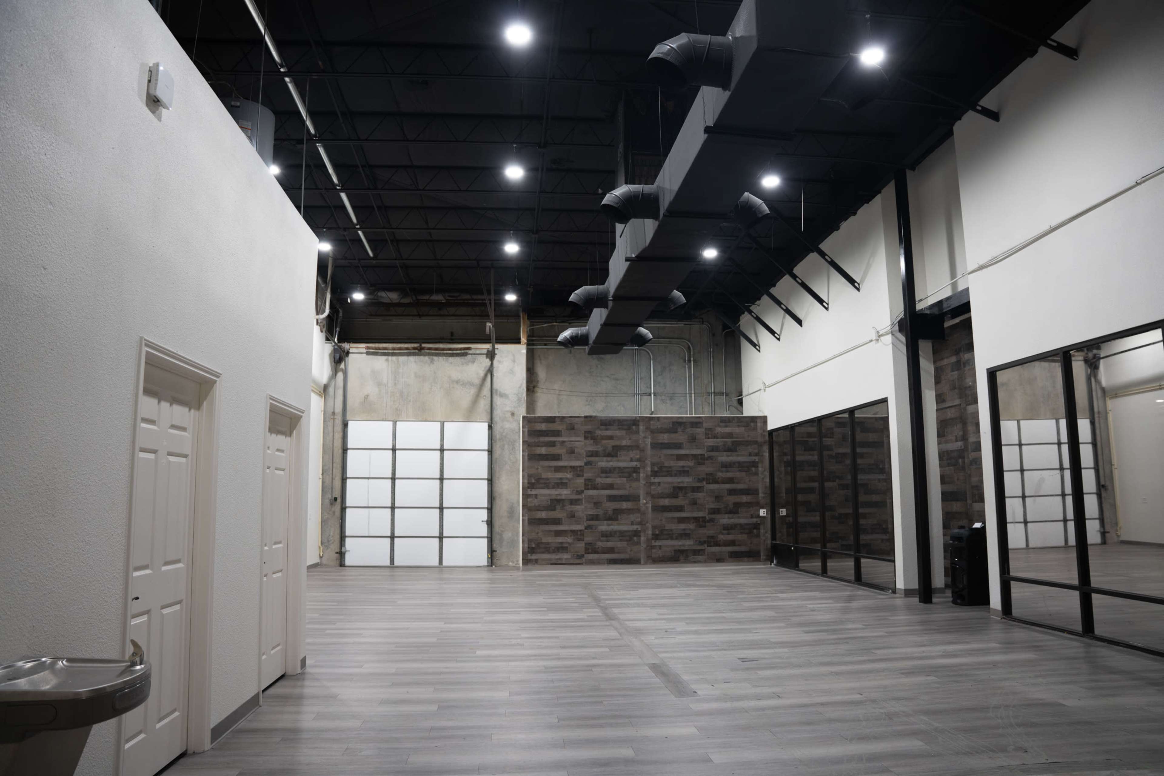 An empty, spacious interior with high ceilings, grey wooden flooring, and a series of large mirrors on one side.
