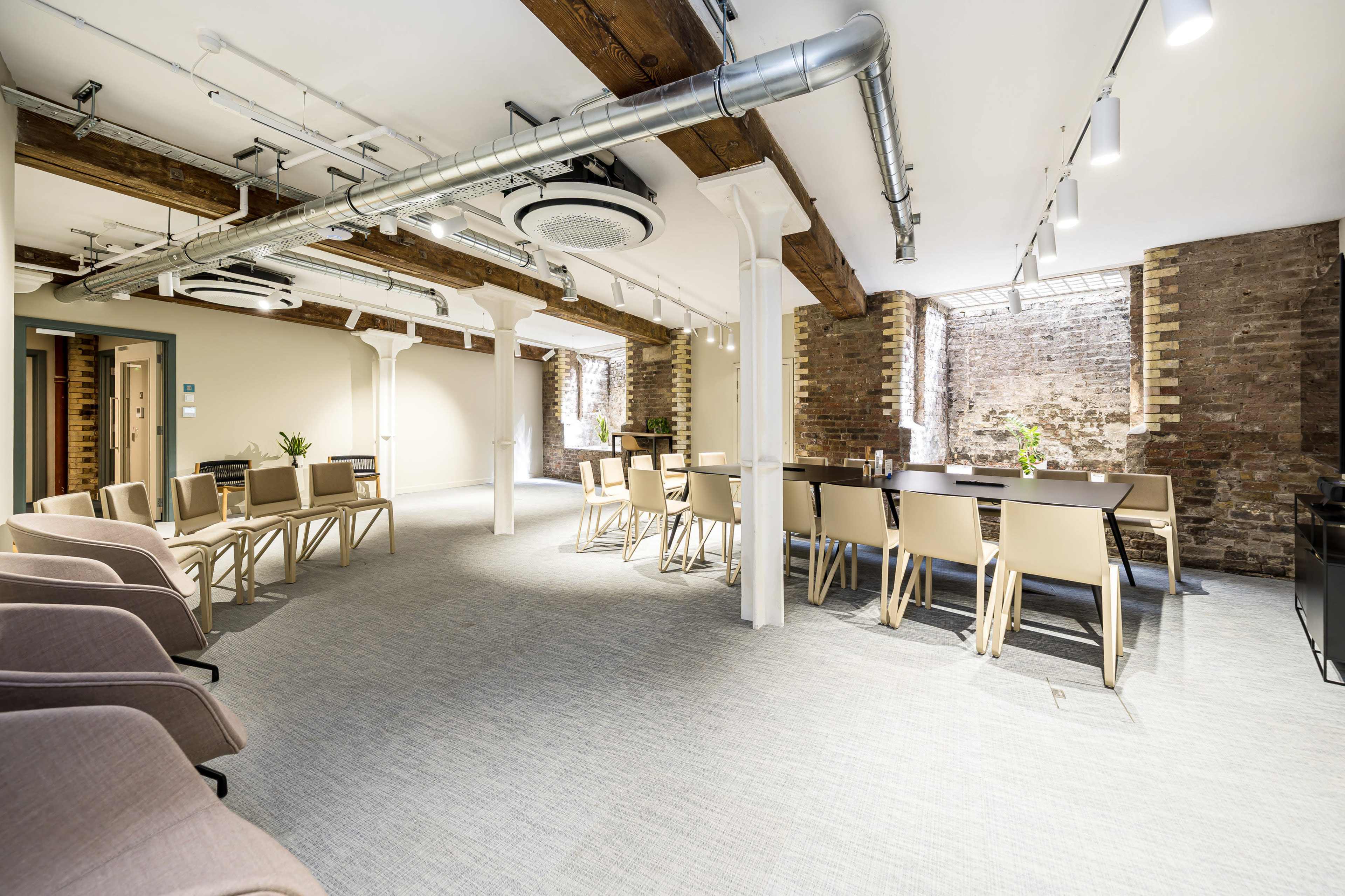 The image shows a modern meeting room with wooden beams, a long conference table, several chairs, and large windows providing natural light.
