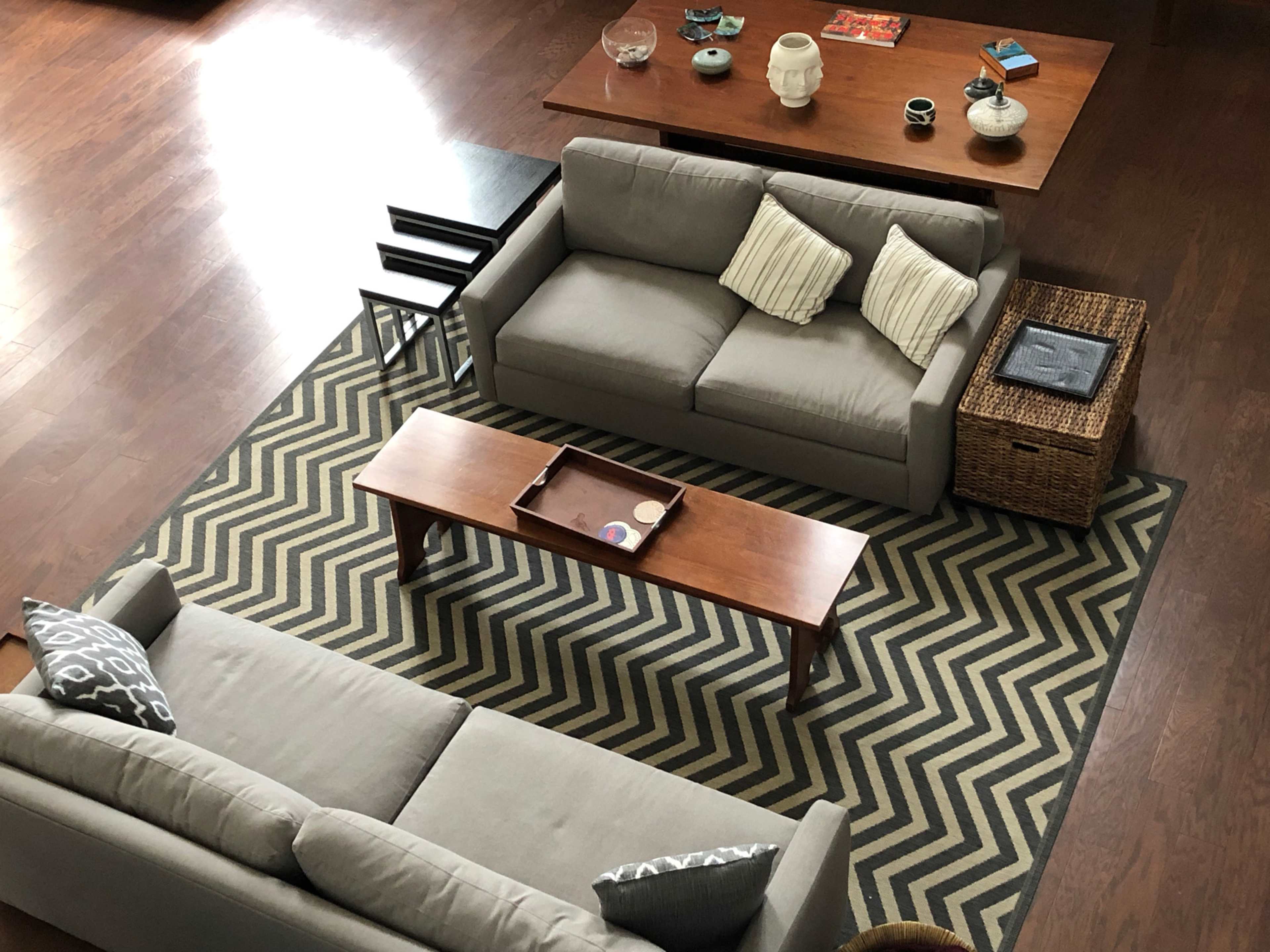 A living room with two gray sofas facing a wooden coffee table on a zigzag patterned rug, surrounded by various decorative items on a nearby table.