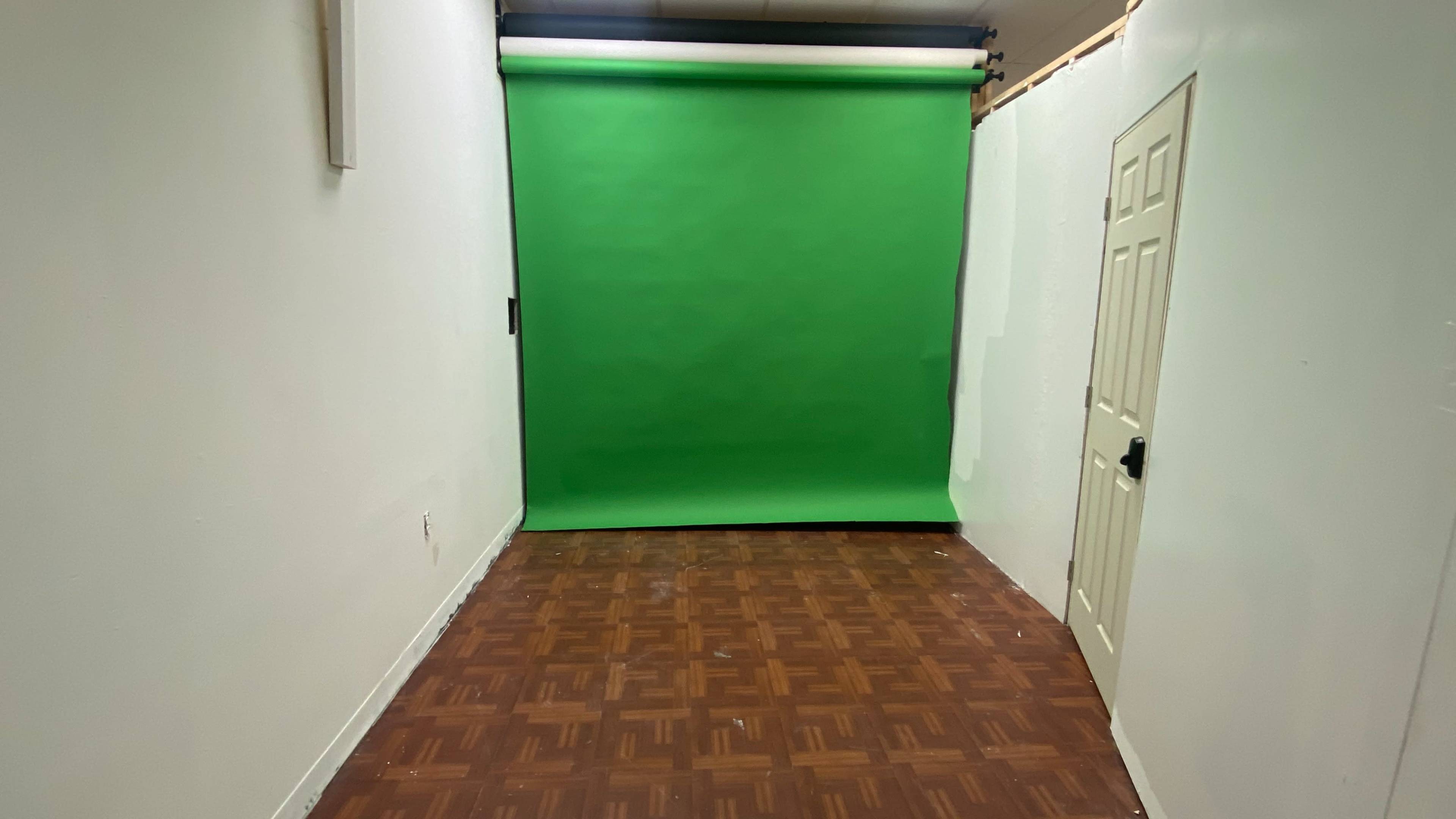 The image shows a room with a green backdrop, wooden flooring, and a closed door on one side.