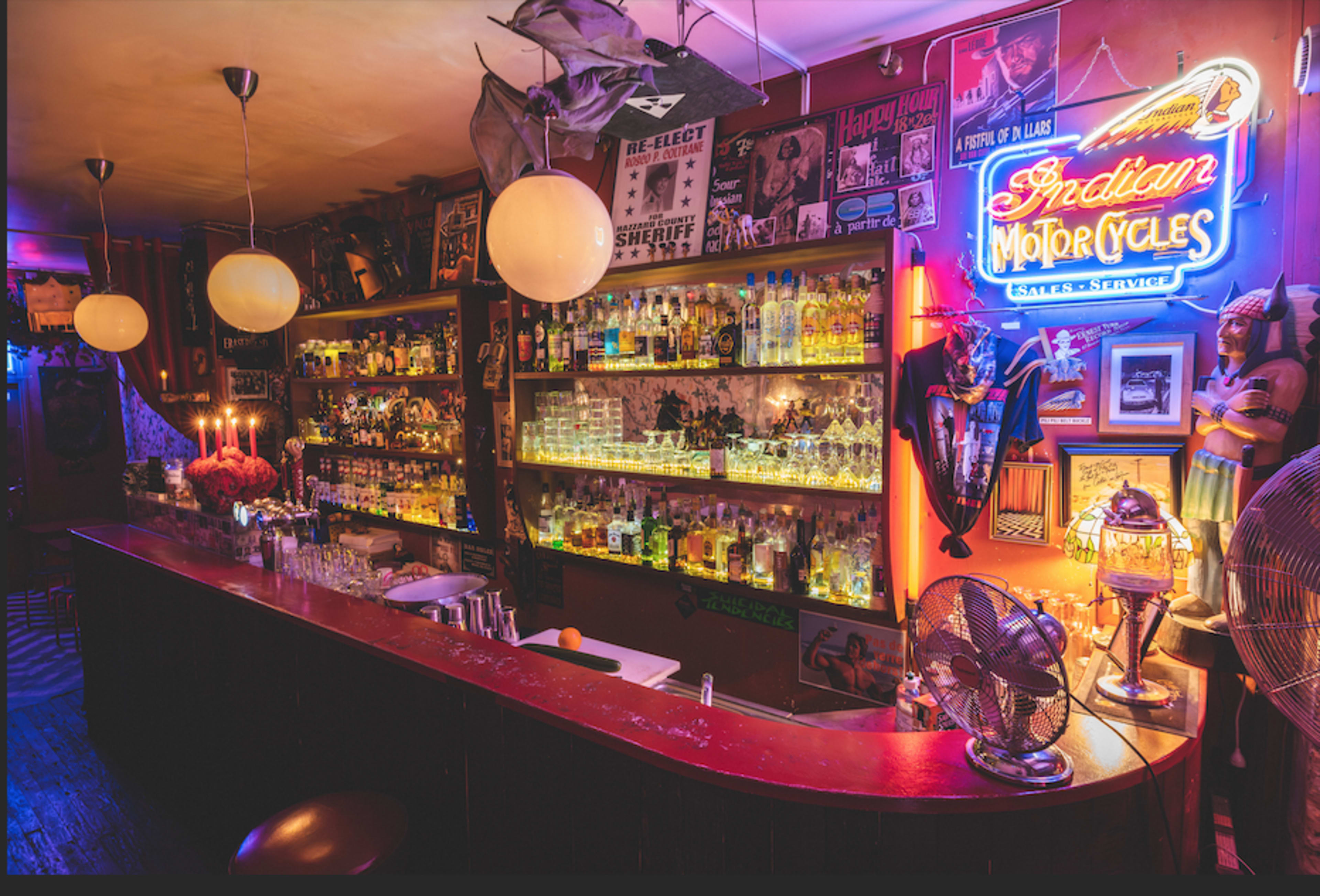 A dimly lit bar with a curved counter, shelves filled with bottles, and neon signage in a vibrant atmosphere.