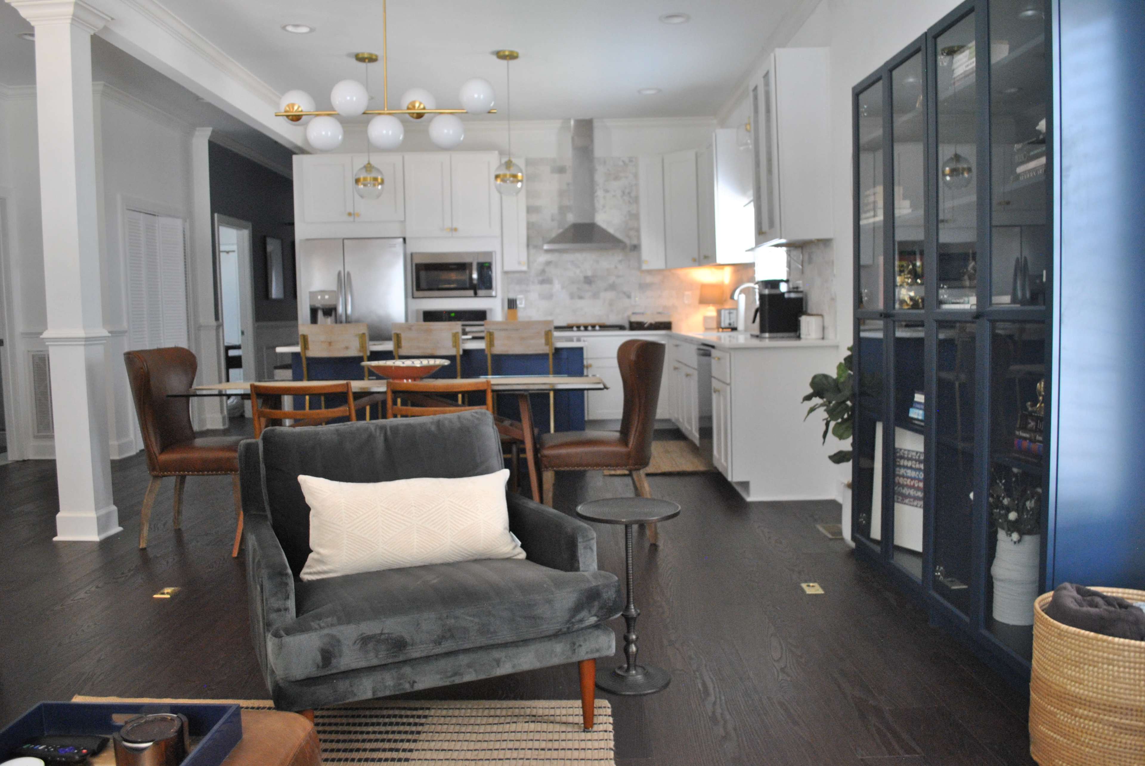 A modern open-concept kitchen and dining area with a seating arrangement that includes a gray armchair and a wooden dining table surrounded by chairs.