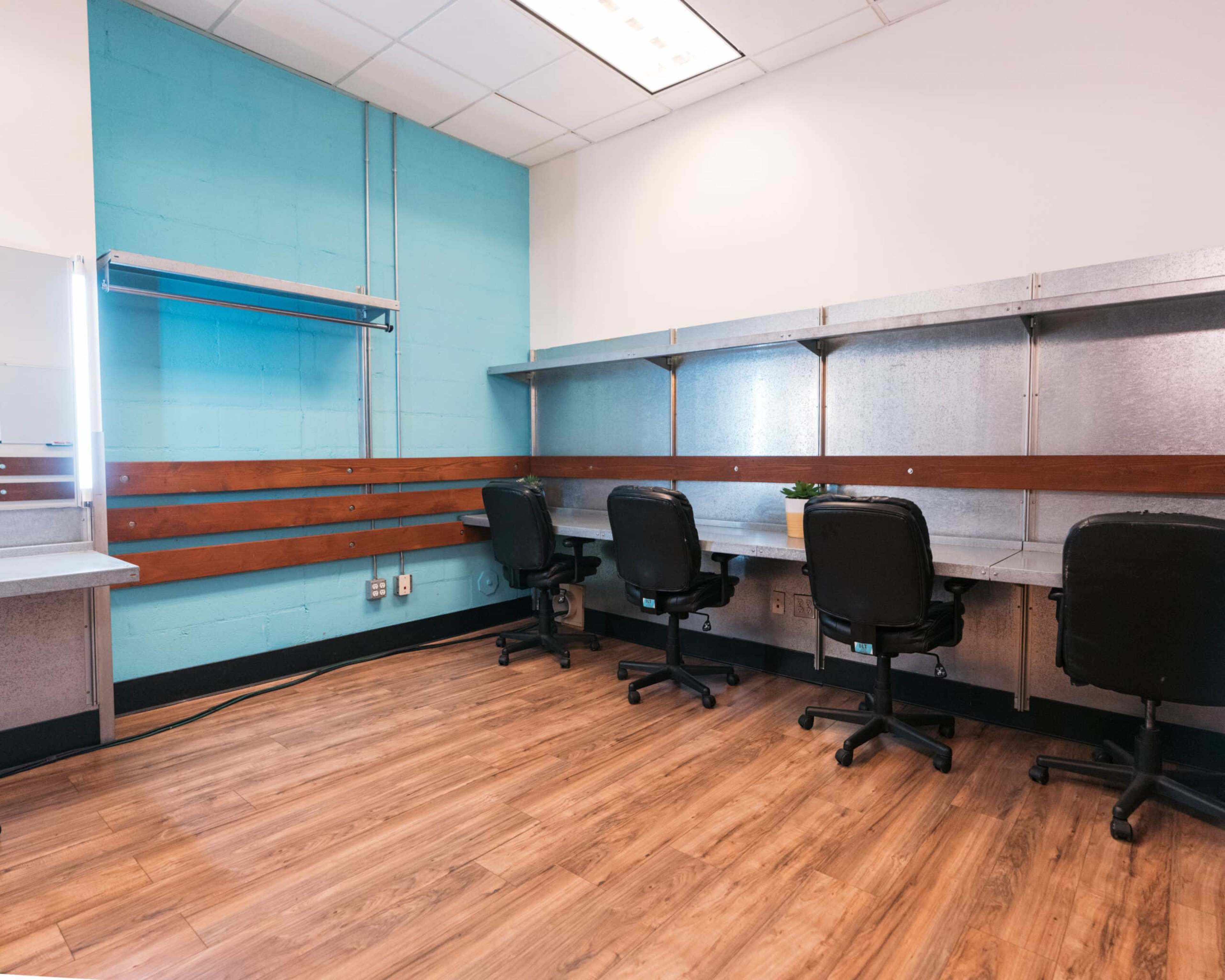 The image shows a modern workspace with three black office chairs arranged at individual desks against a turquoise wall.