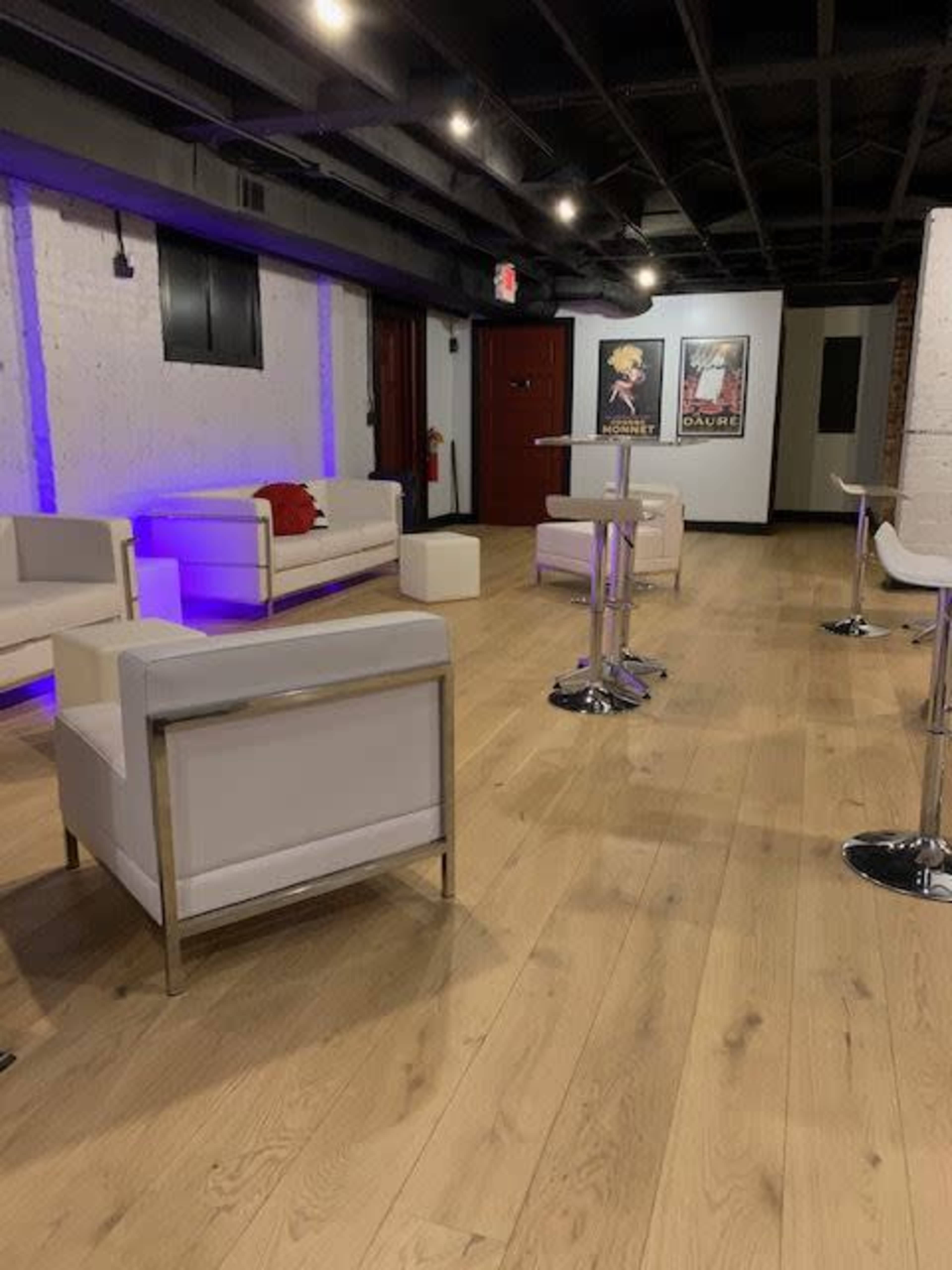 A modern interior with white furniture, including a couch and bar tables, set against a wooden floor and soft purple lighting.