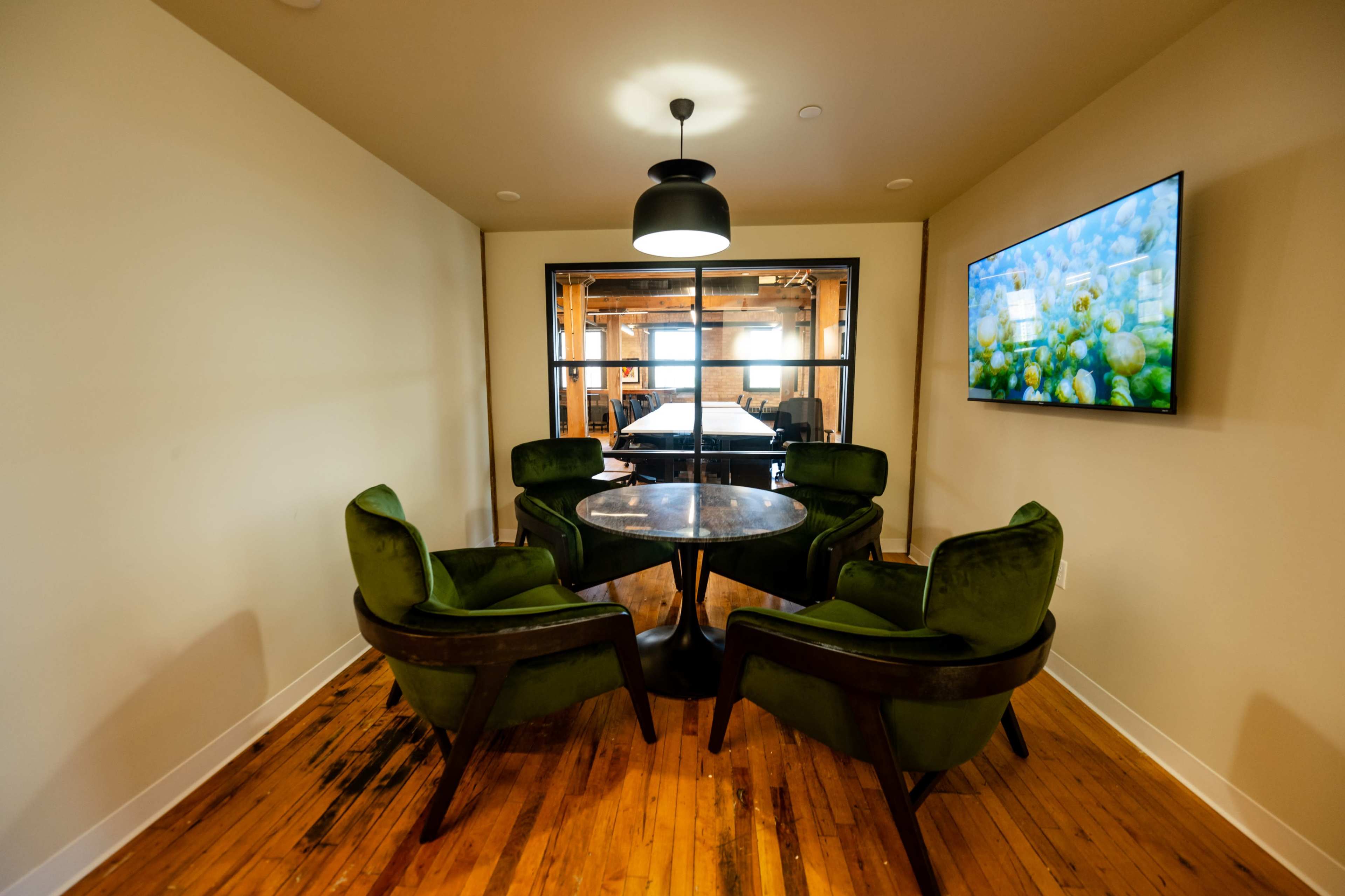 A small seating area features four green chairs surrounding a round glass table, with a large window and a television mounted on the wall nearby.