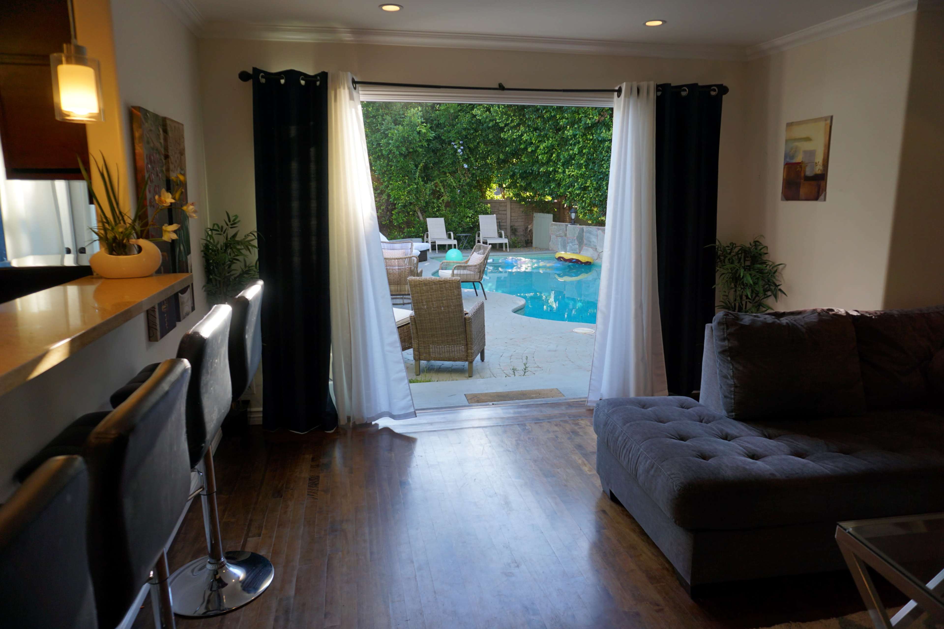 A cozy living room opens up to a pool area through large glass doors, revealing outdoor seating and a well-maintained pool.