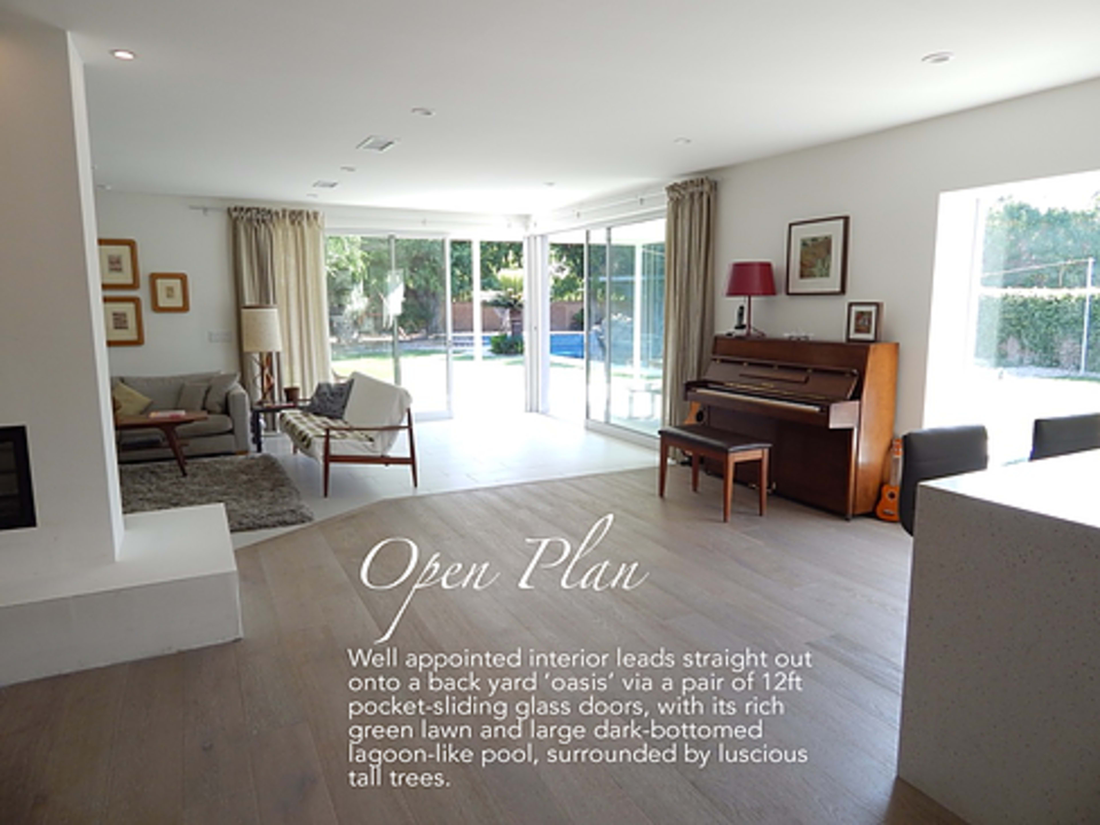 A bright, open interior space that connects to a backyard with a pool and tall trees visible through large sliding glass doors.