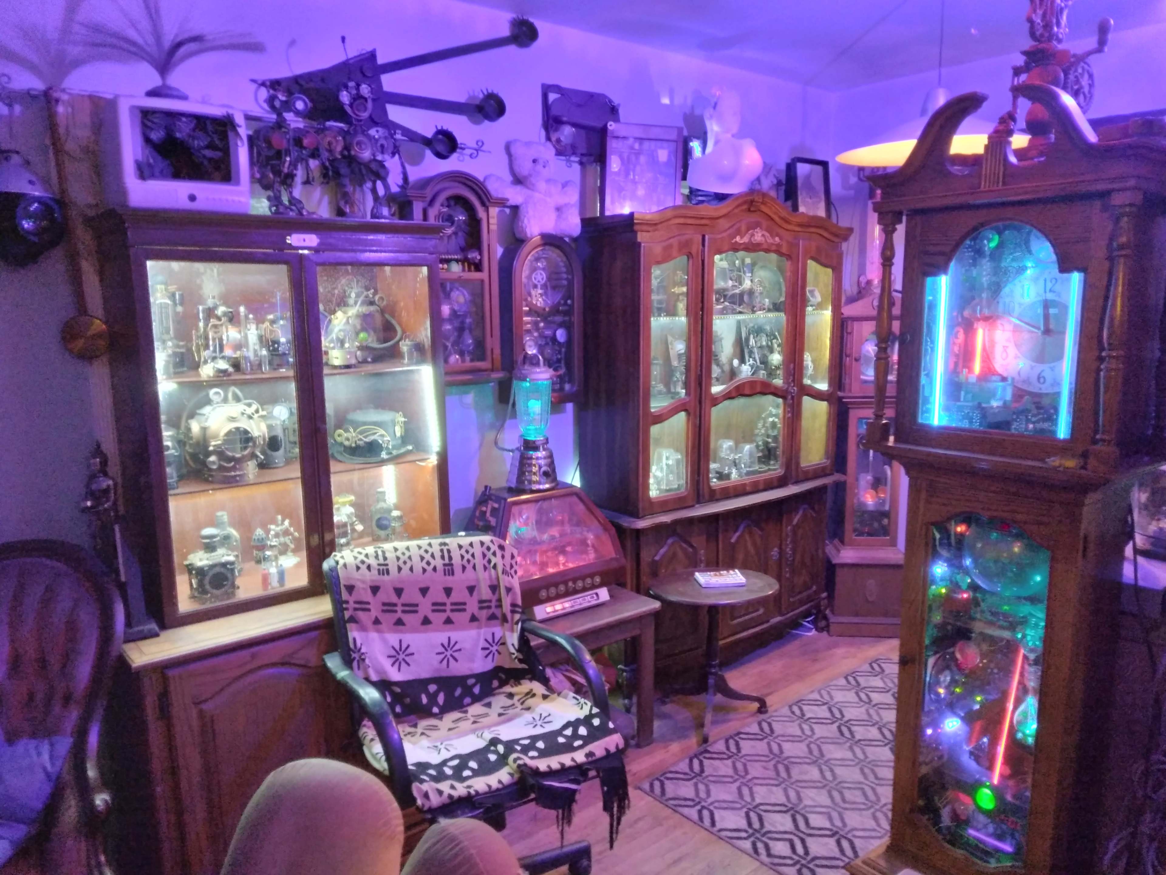 The room features multiple glass display cabinets filled with various vintage collectibles, surrounded by ornate furniture and illuminated by colored lighting.