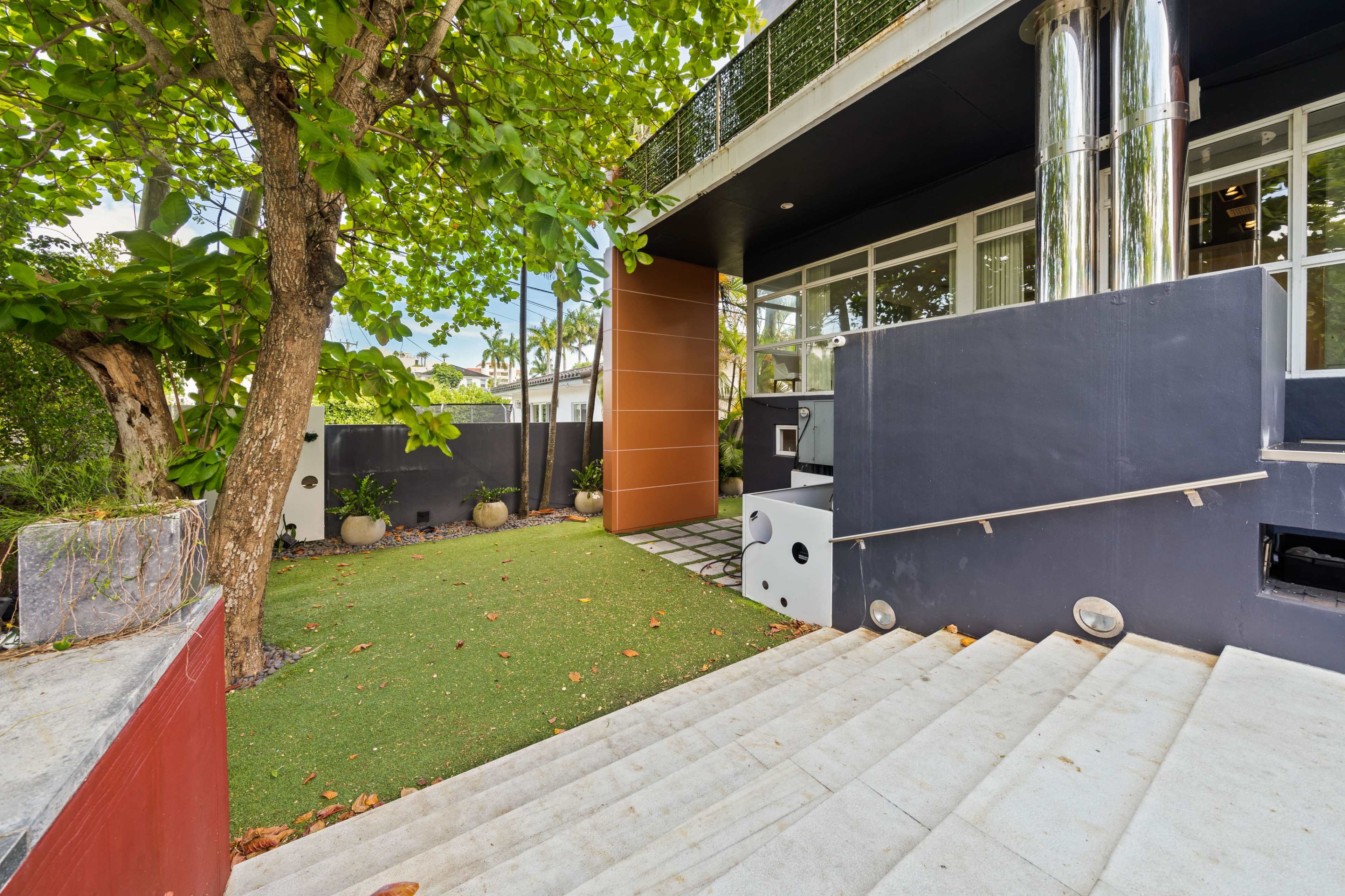 A pathway with concrete steps leads to a modern building entryway surrounded by greenery and decorative planters.