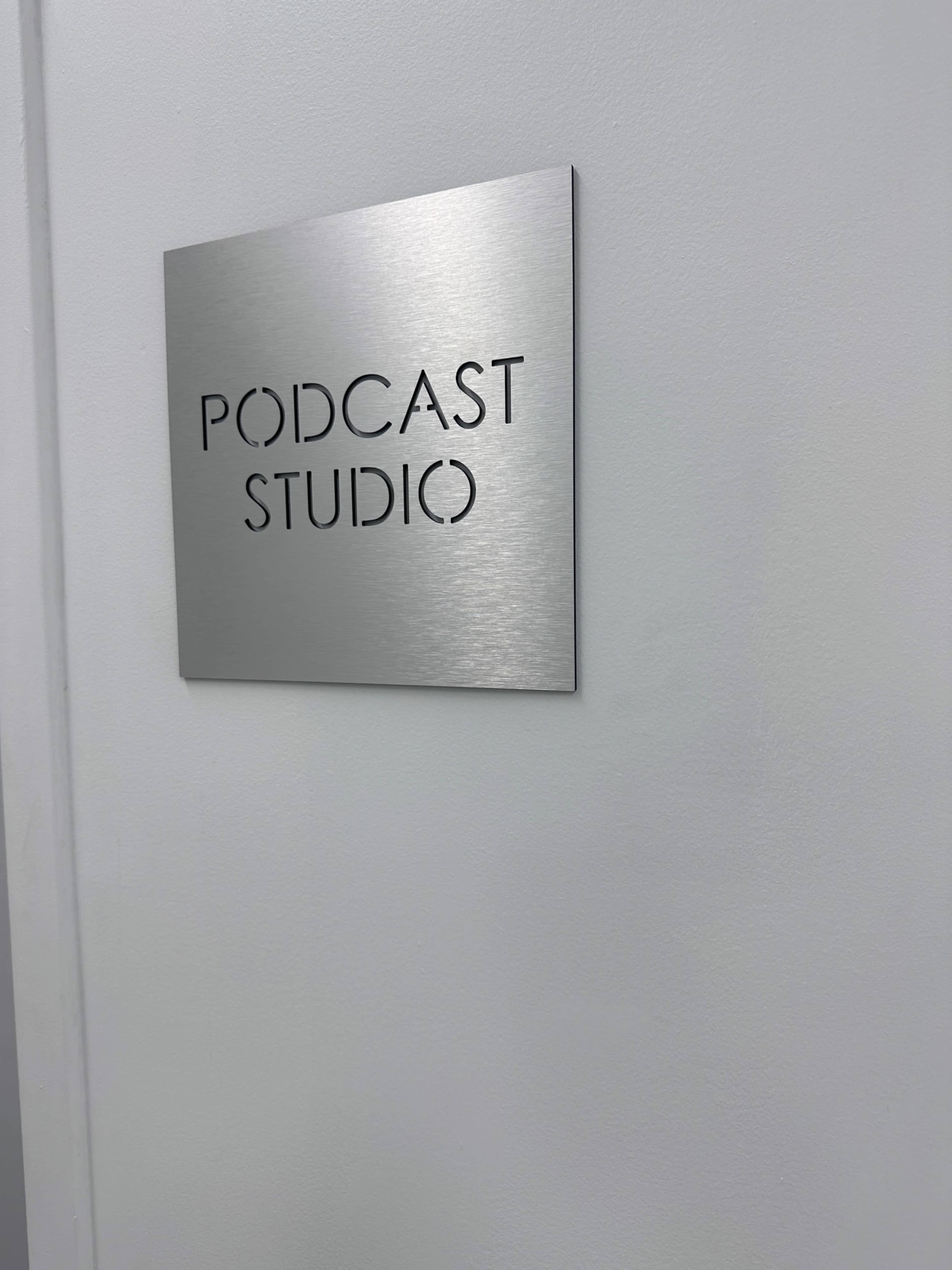 A brushed metal sign labeled "PODCAST STUDIO" is mounted on a white wall.