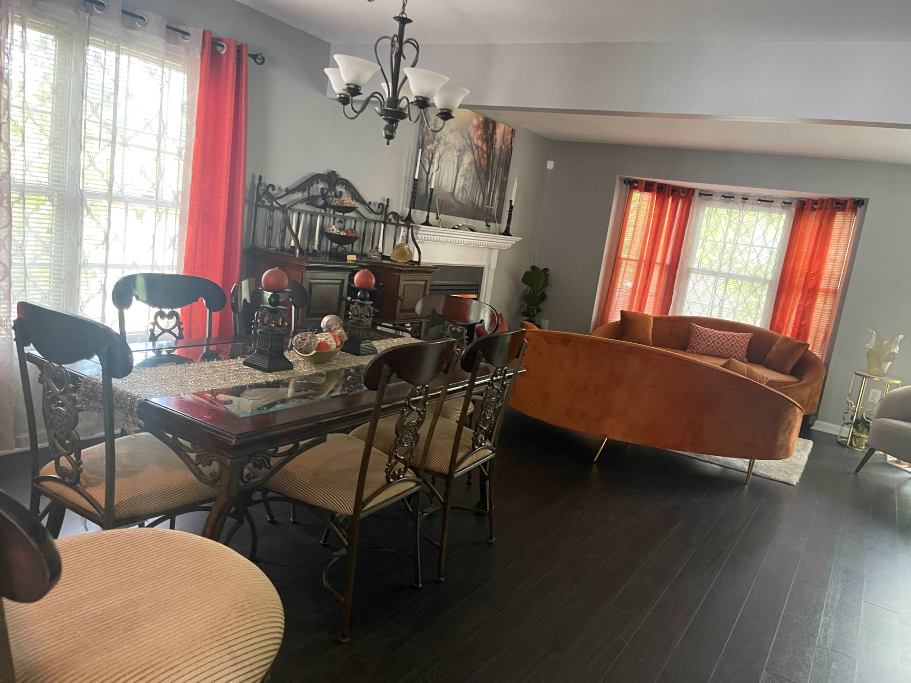 A dining area with a table surrounded by chairs, a chandelier above, and a cozy living area featuring a curved orange sofa.