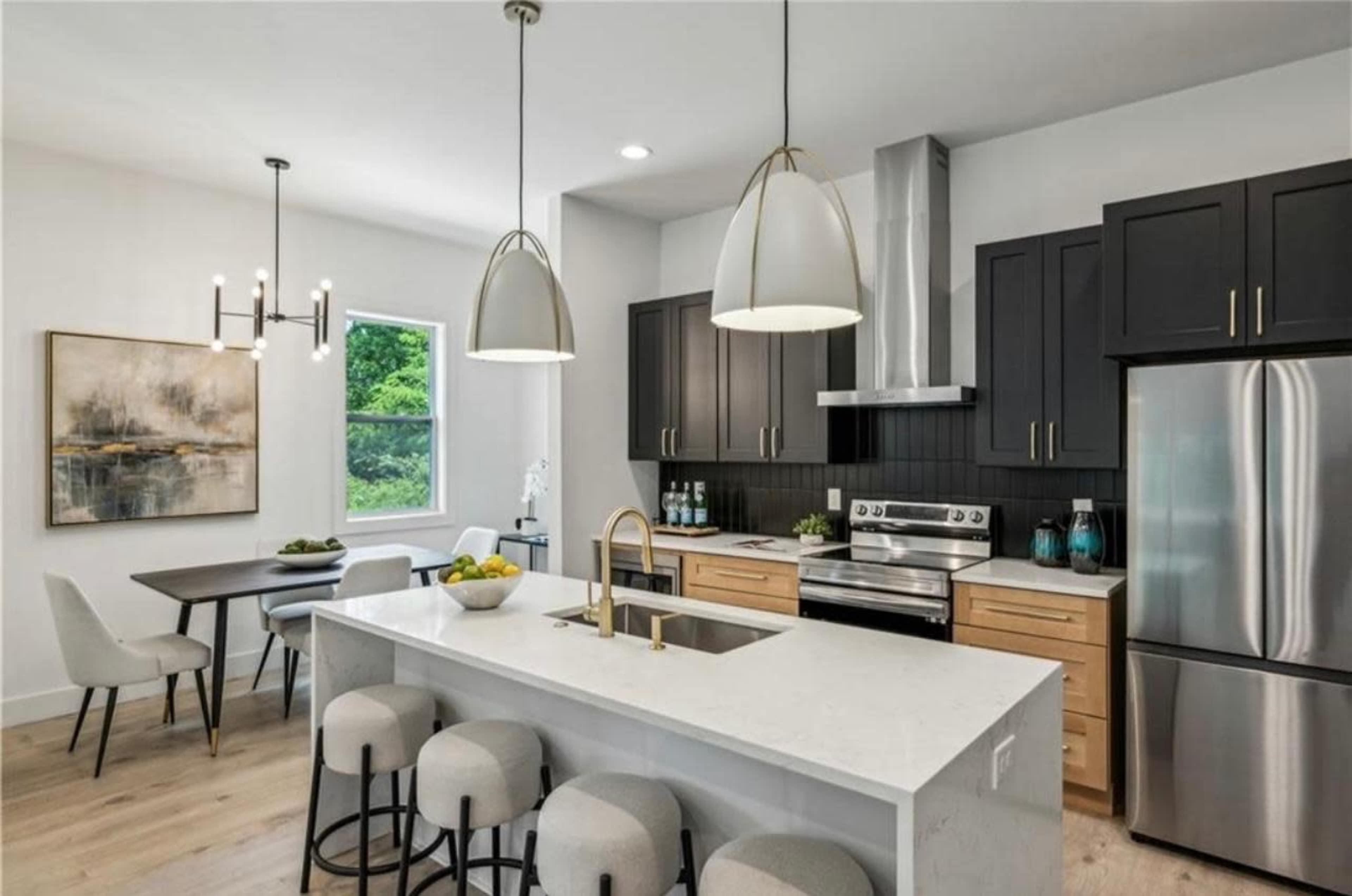 The image shows a modern kitchen featuring dark cabinetry, a large island with bar stools, stainless steel appliances, and a dining area with a table and chairs.