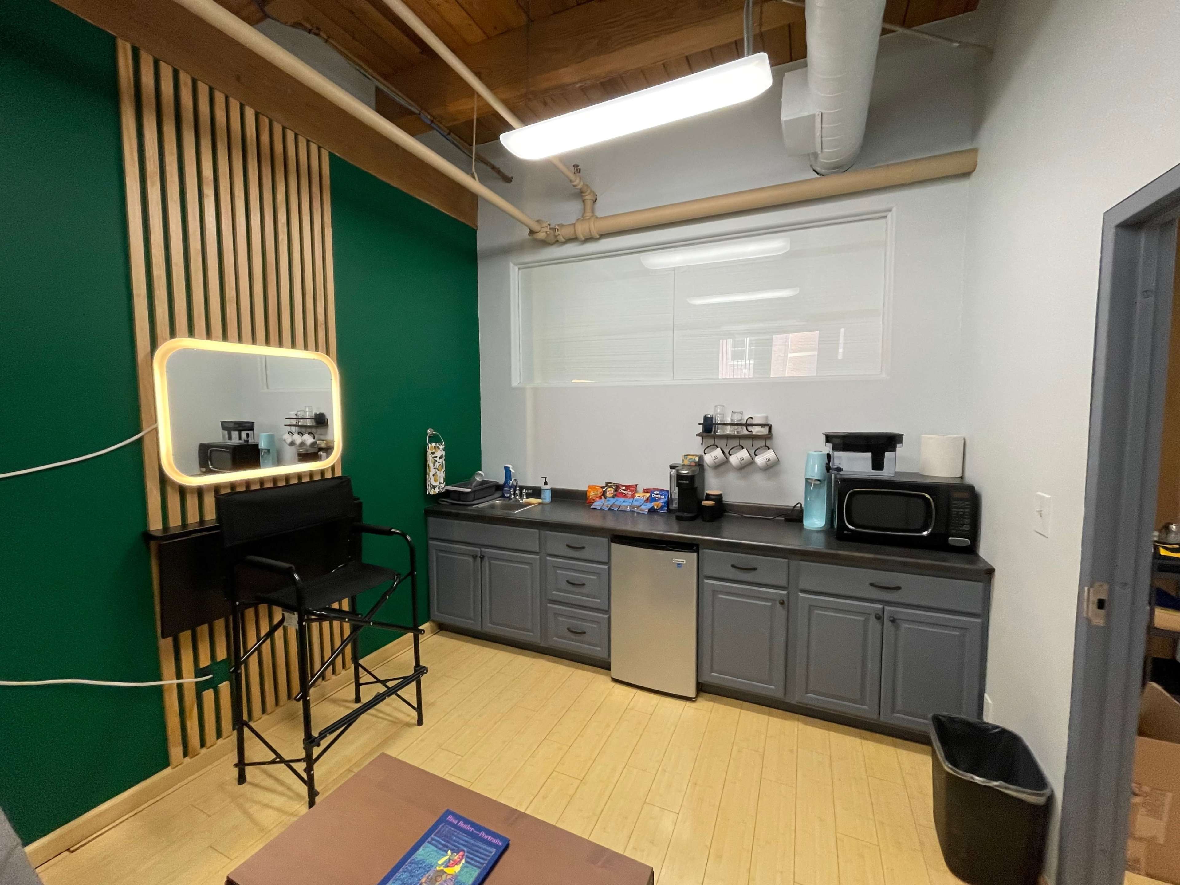 A modern kitchen space with a green accent wall, equipped with a sink, countertop appliances, and gray cabinetry.