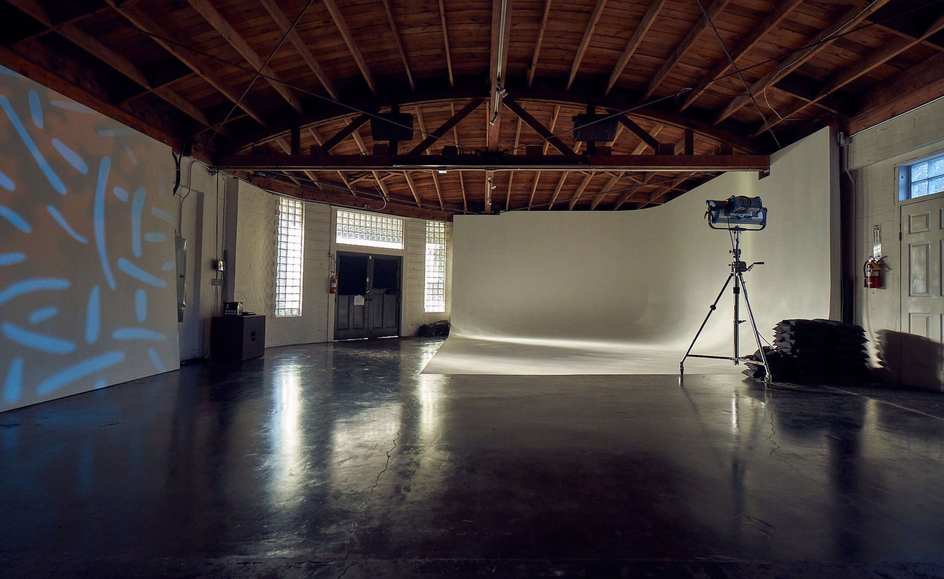 A photography studio features a seamless backdrop, a lighting setup on a tripod, and large windows allowing natural light.