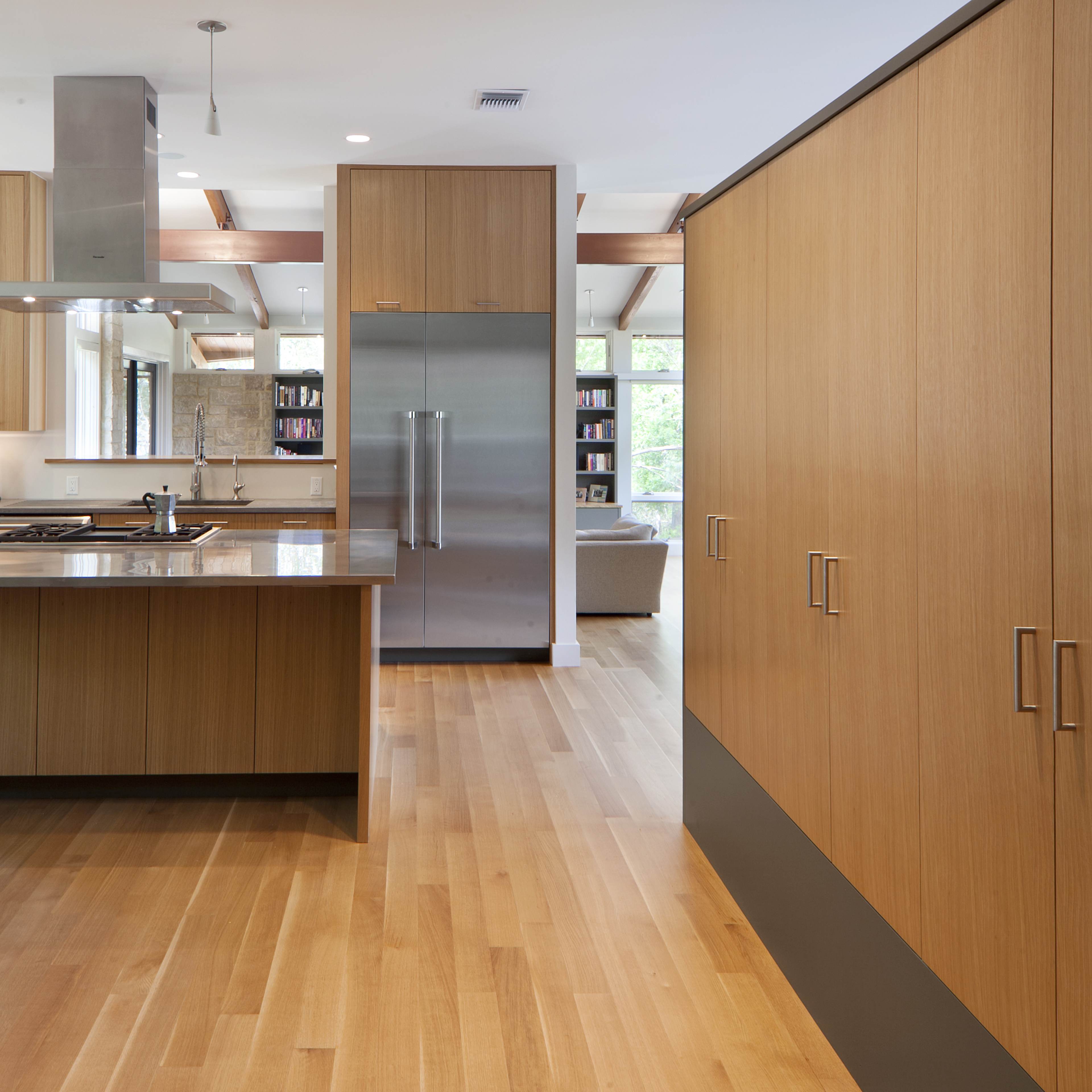 A modern kitchen featuring wooden cabinetry, a stainless steel refrigerator, and hardwood flooring.