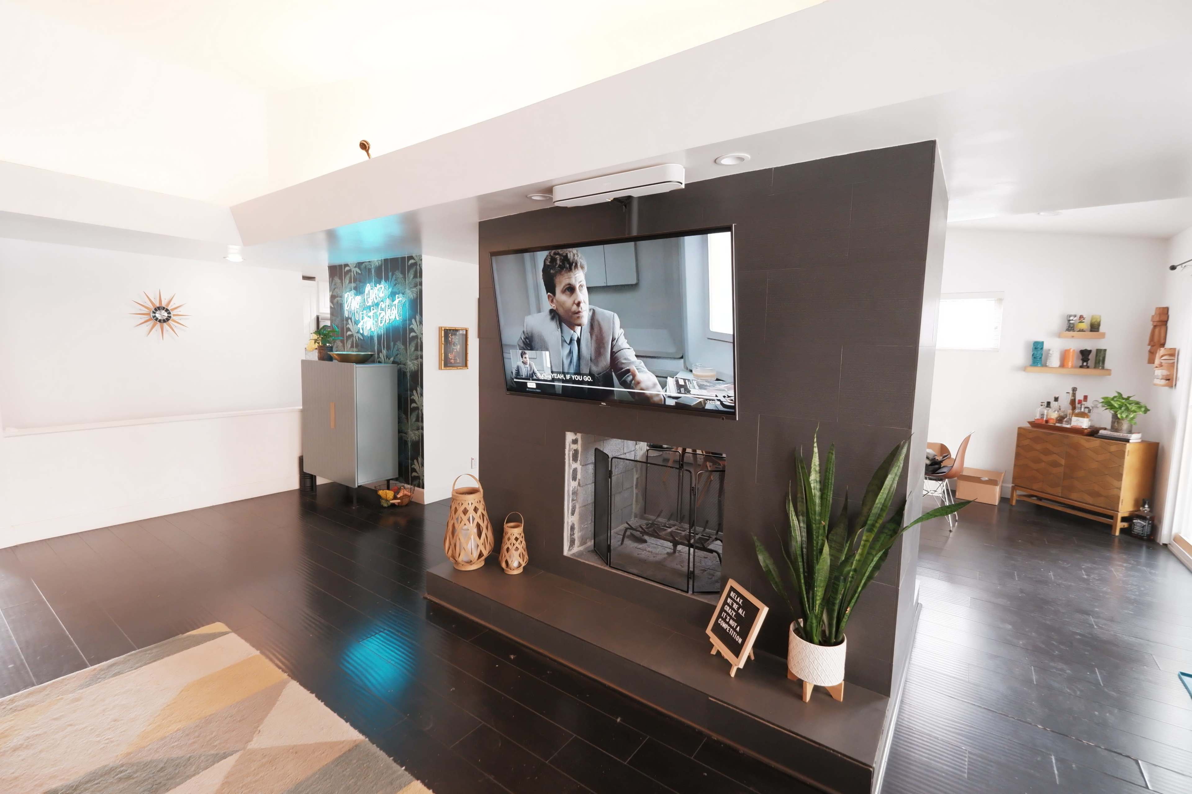 A modern living room with a television mounted on a wall, a fireplace beneath it, and various decorative plants and furniture in the space.