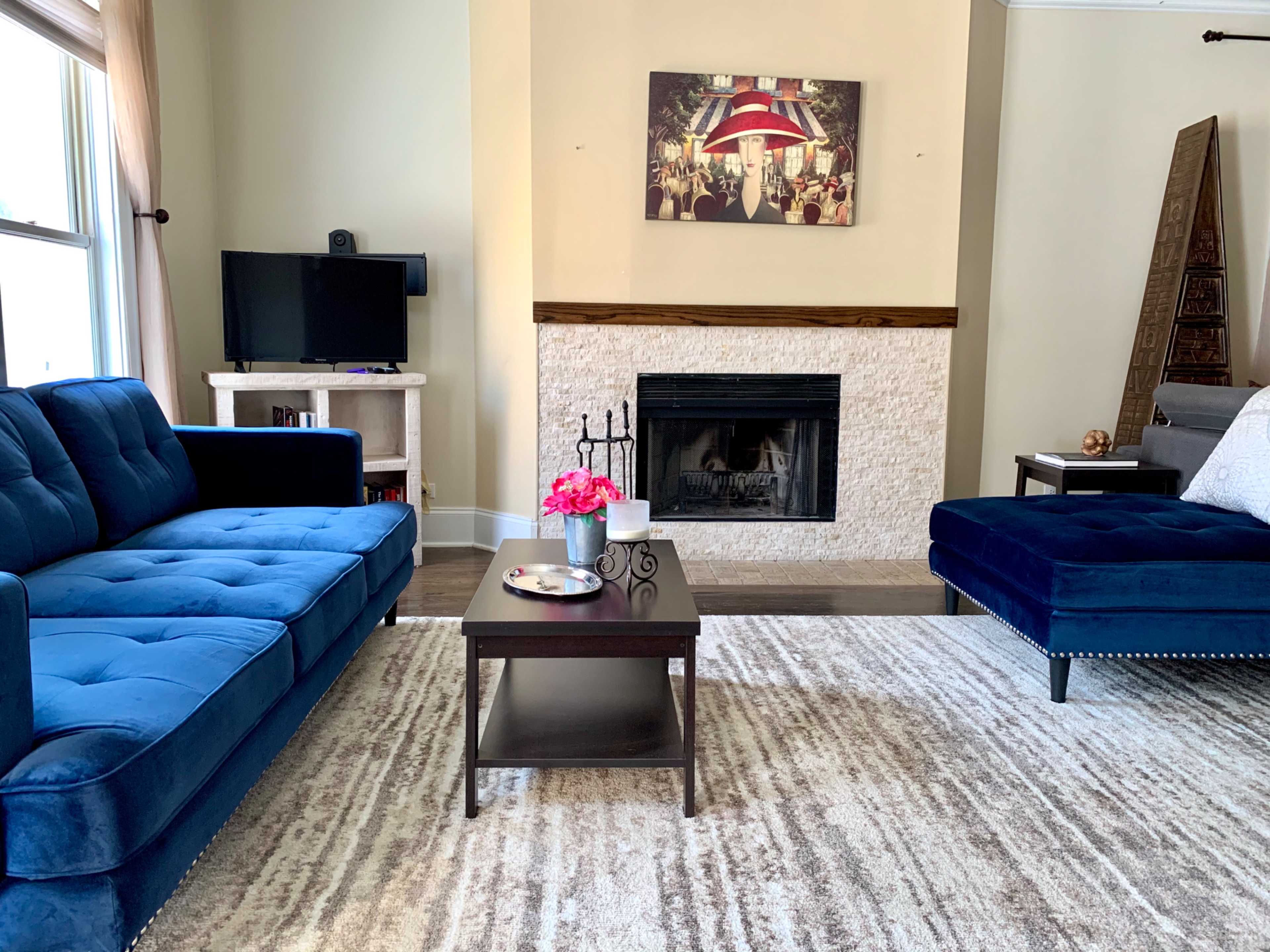 The living room features two blue sofas facing a coffee table, a fireplace, and a wall-mounted television under a framed artwork.