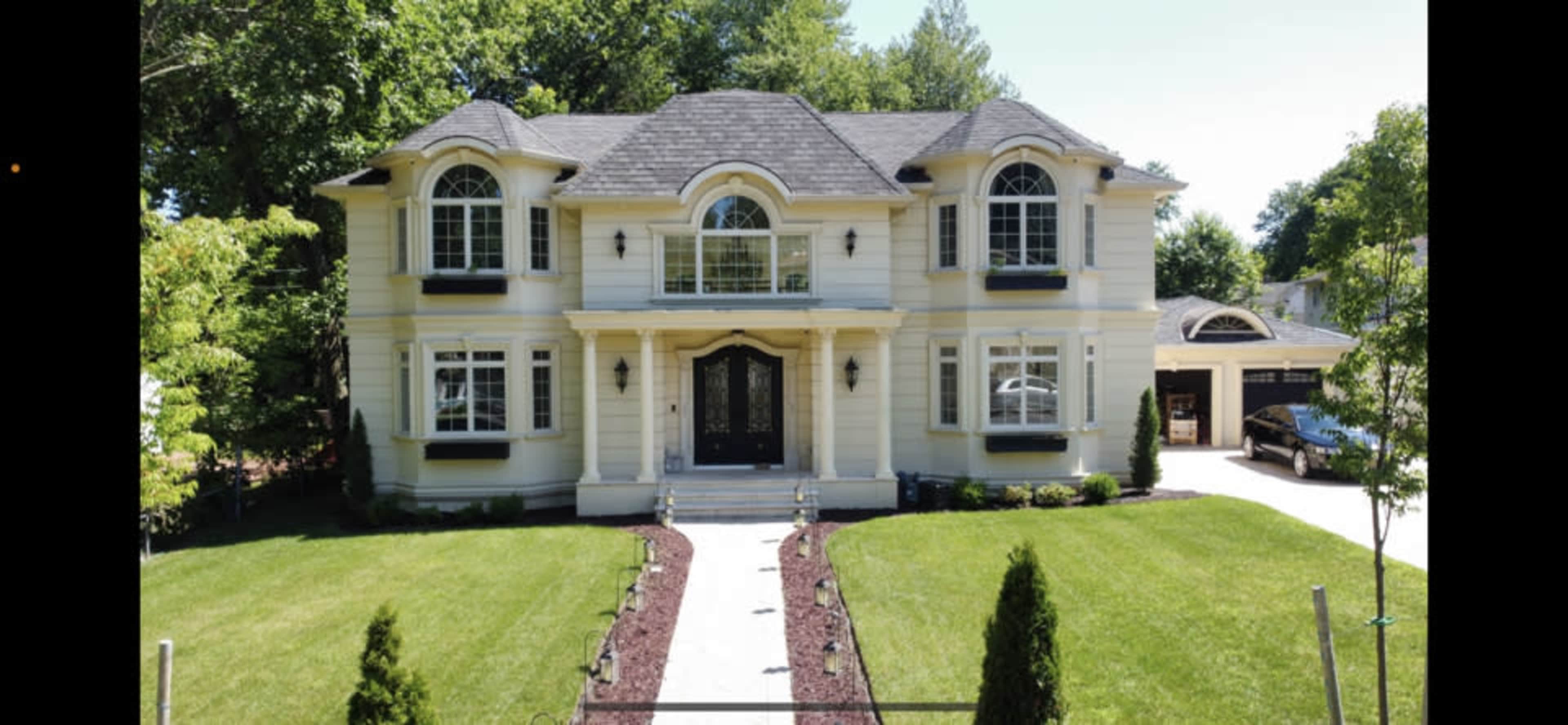A two-story house with white siding, large windows, and a well-manicured lawn, accompanied by a paved walkway leading to the entrance.