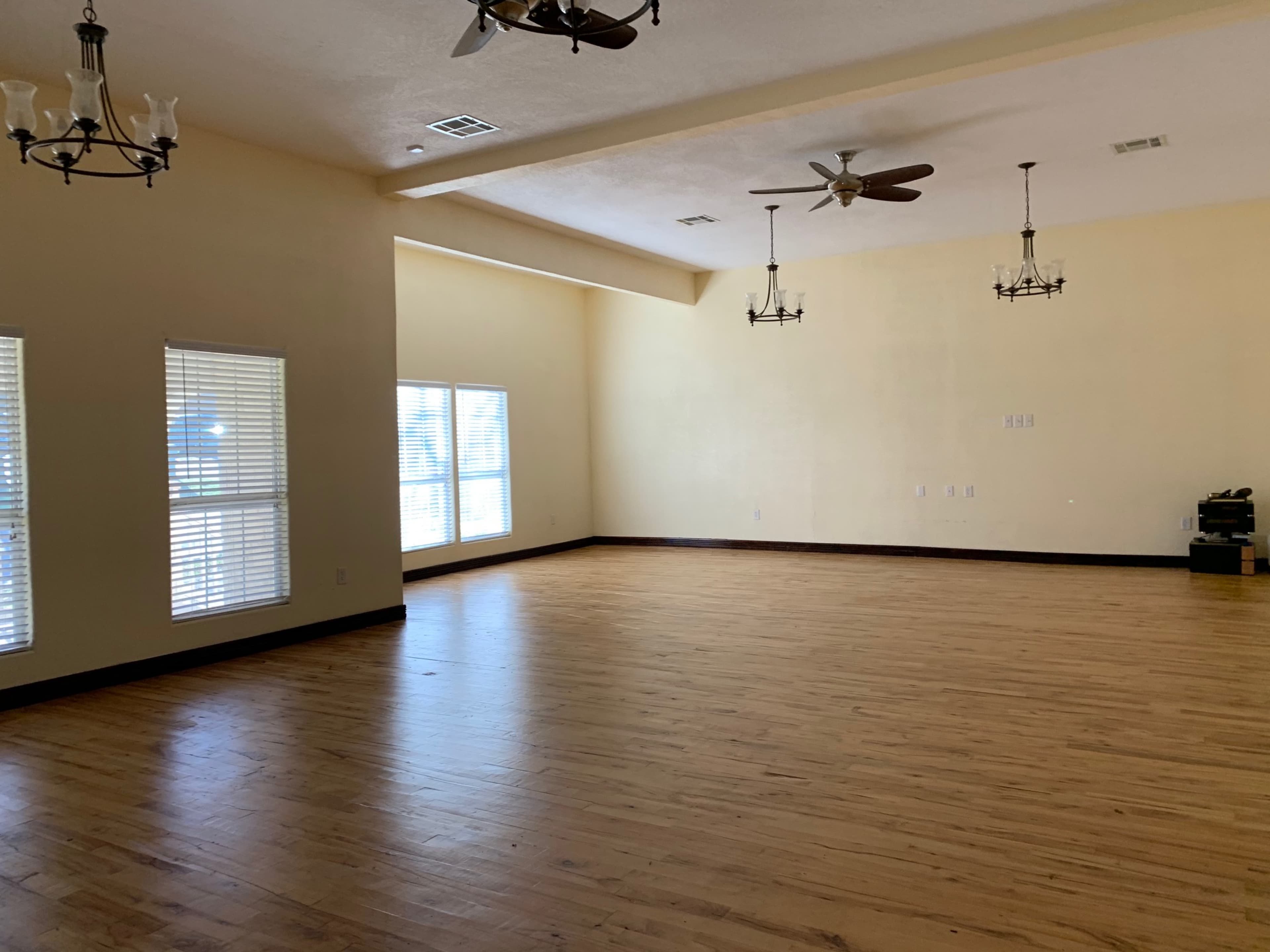 A spacious, empty room with wooden floors, tall ceilings, and several ceiling fans.