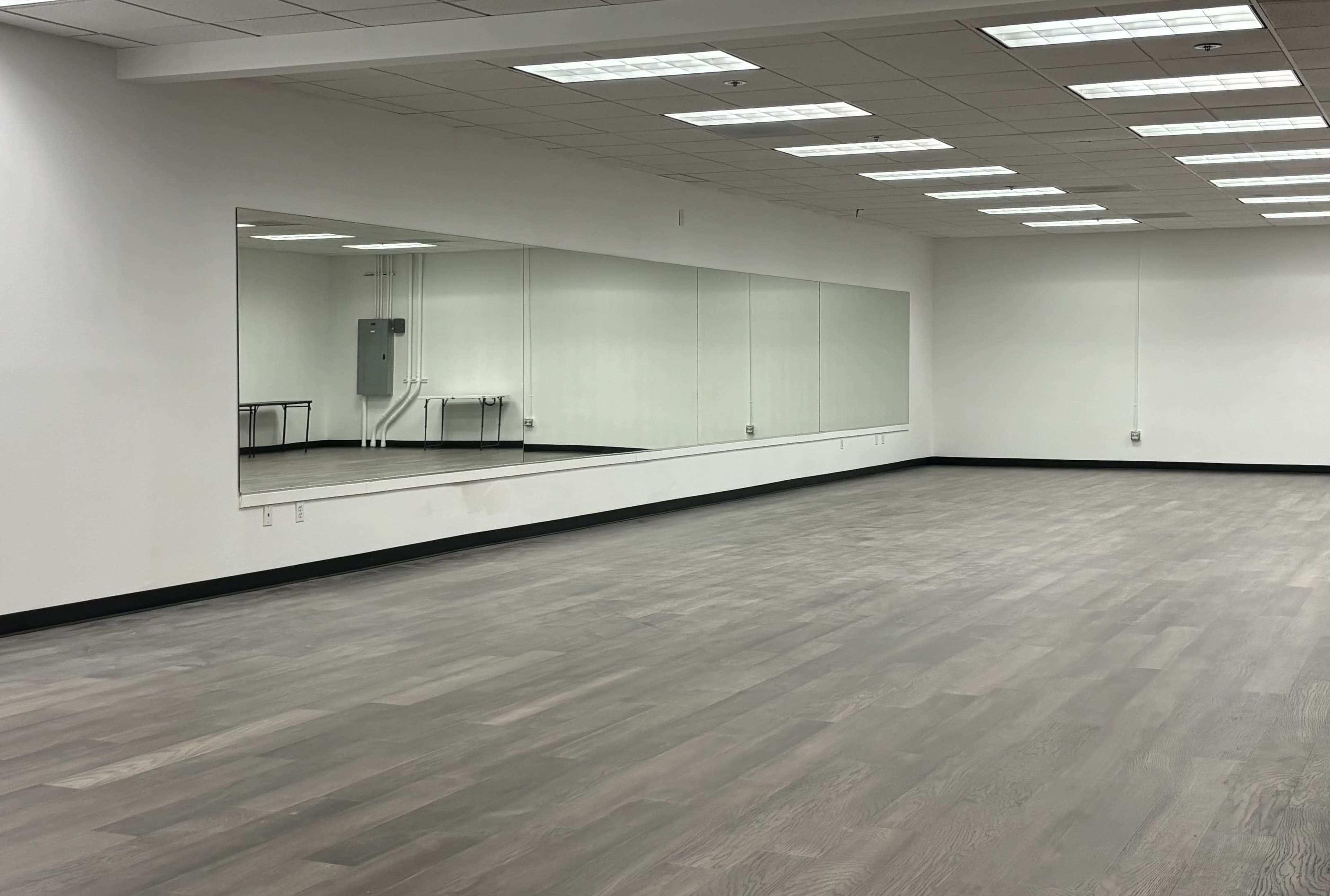 An empty room with light-colored wooden flooring and a large wall mirror.