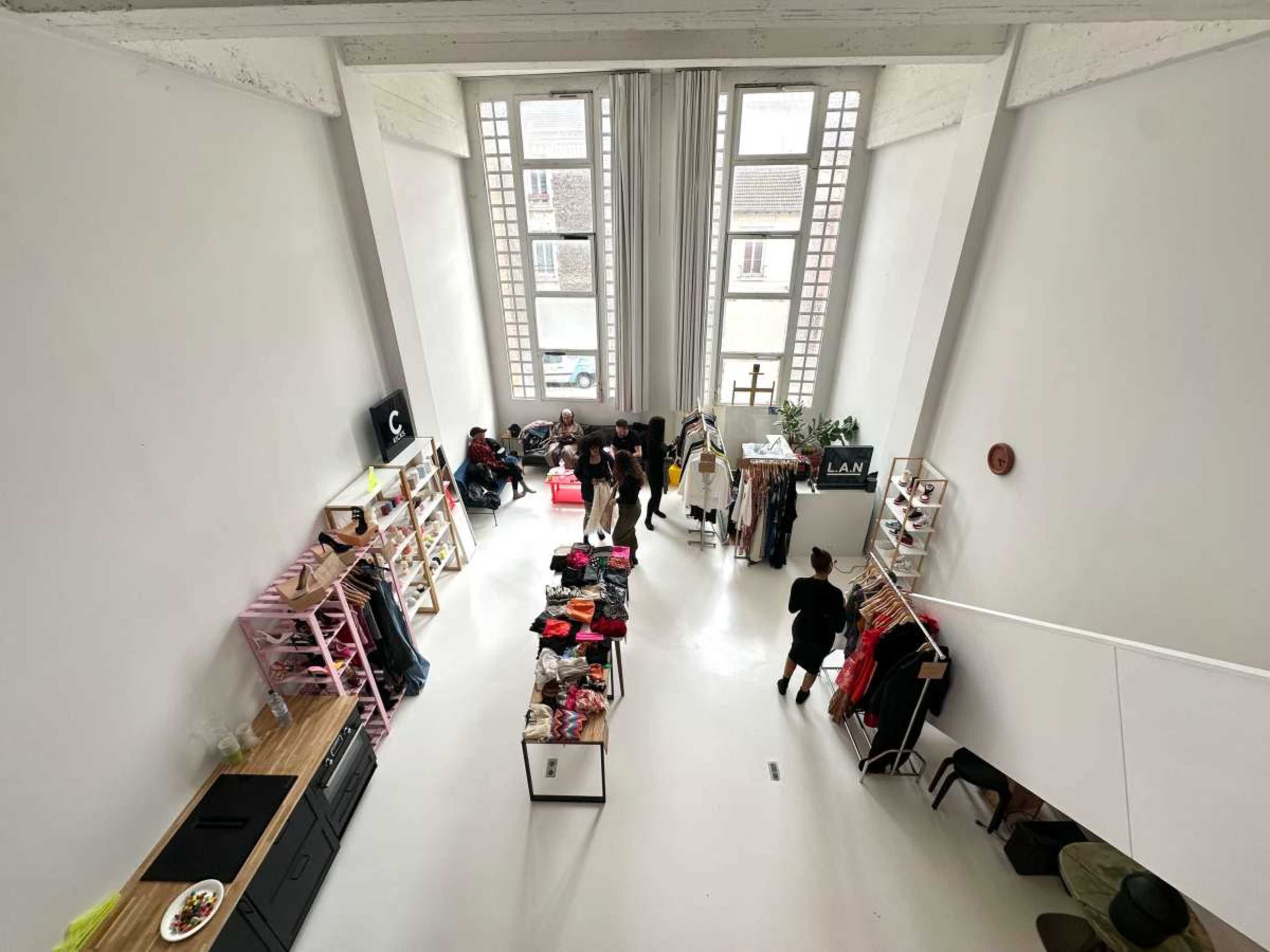 The image shows a spacious retail space with large windows, featuring clothing displays and several people shopping or interacting.