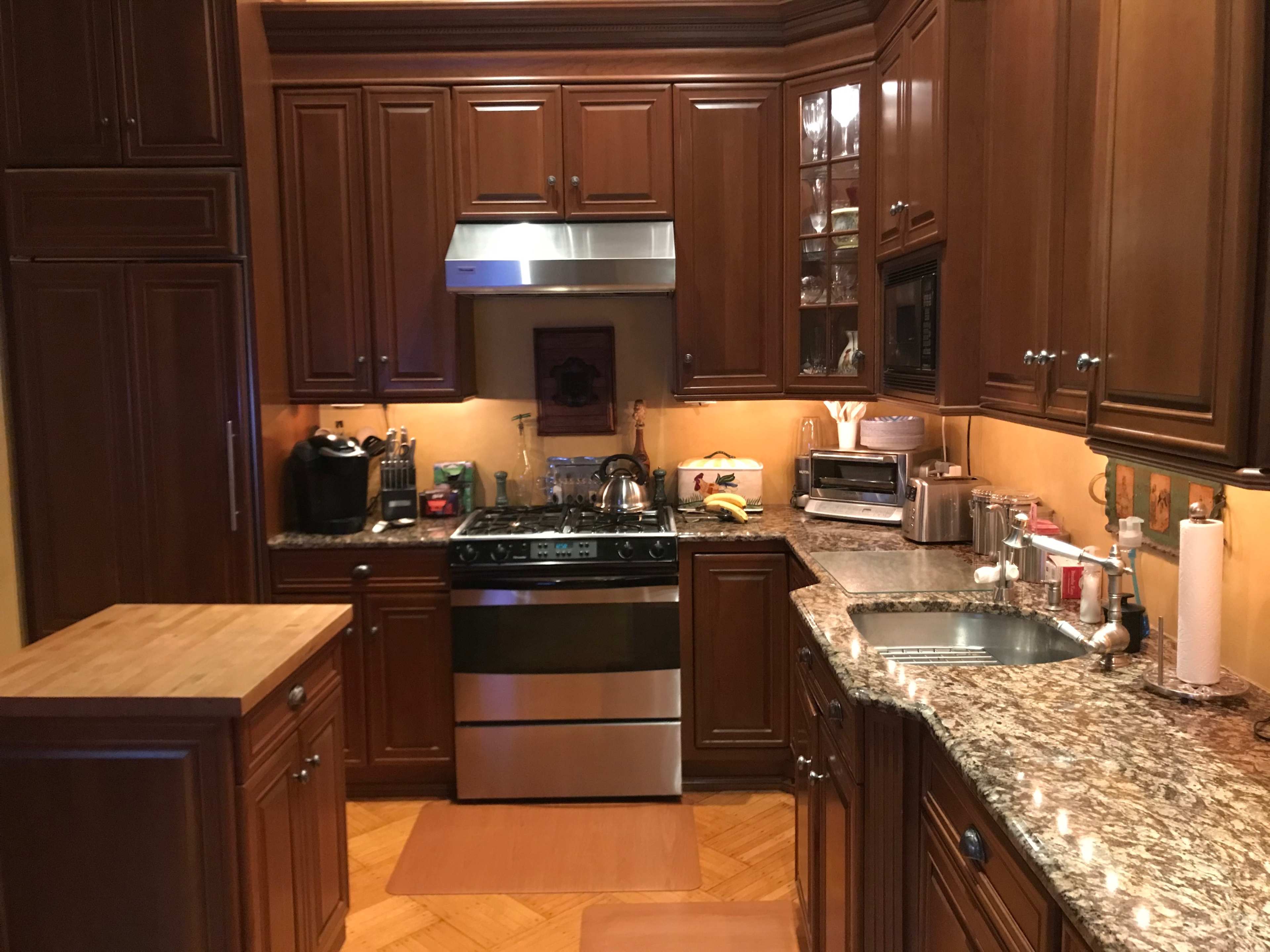 The kitchen features wooden cabinetry, a stainless steel stove, and granite countertops with various appliances visible.