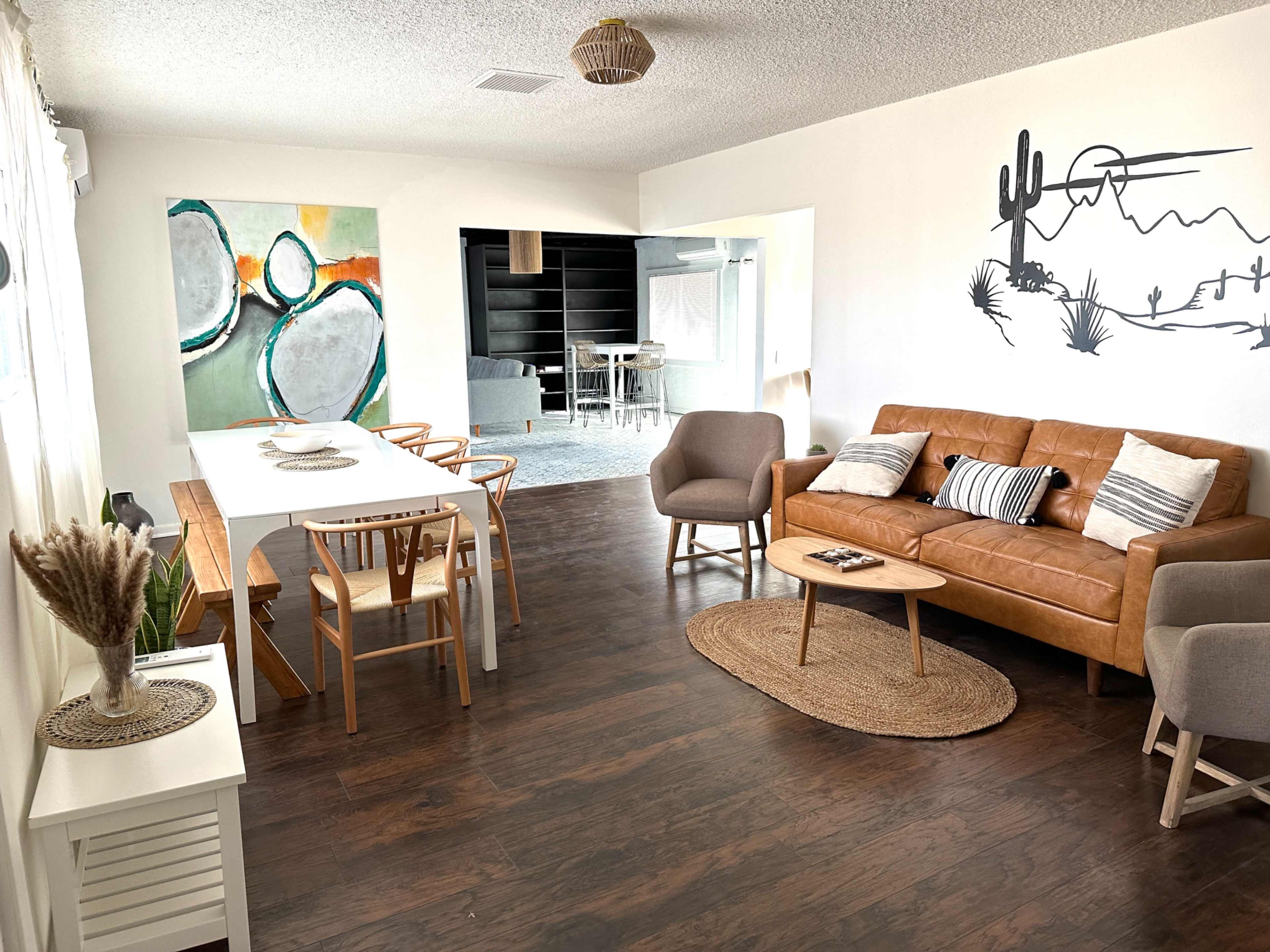 A modern living room and dining area featuring a brown leather sofa, a dining table with wooden chairs, and decorative wall art.