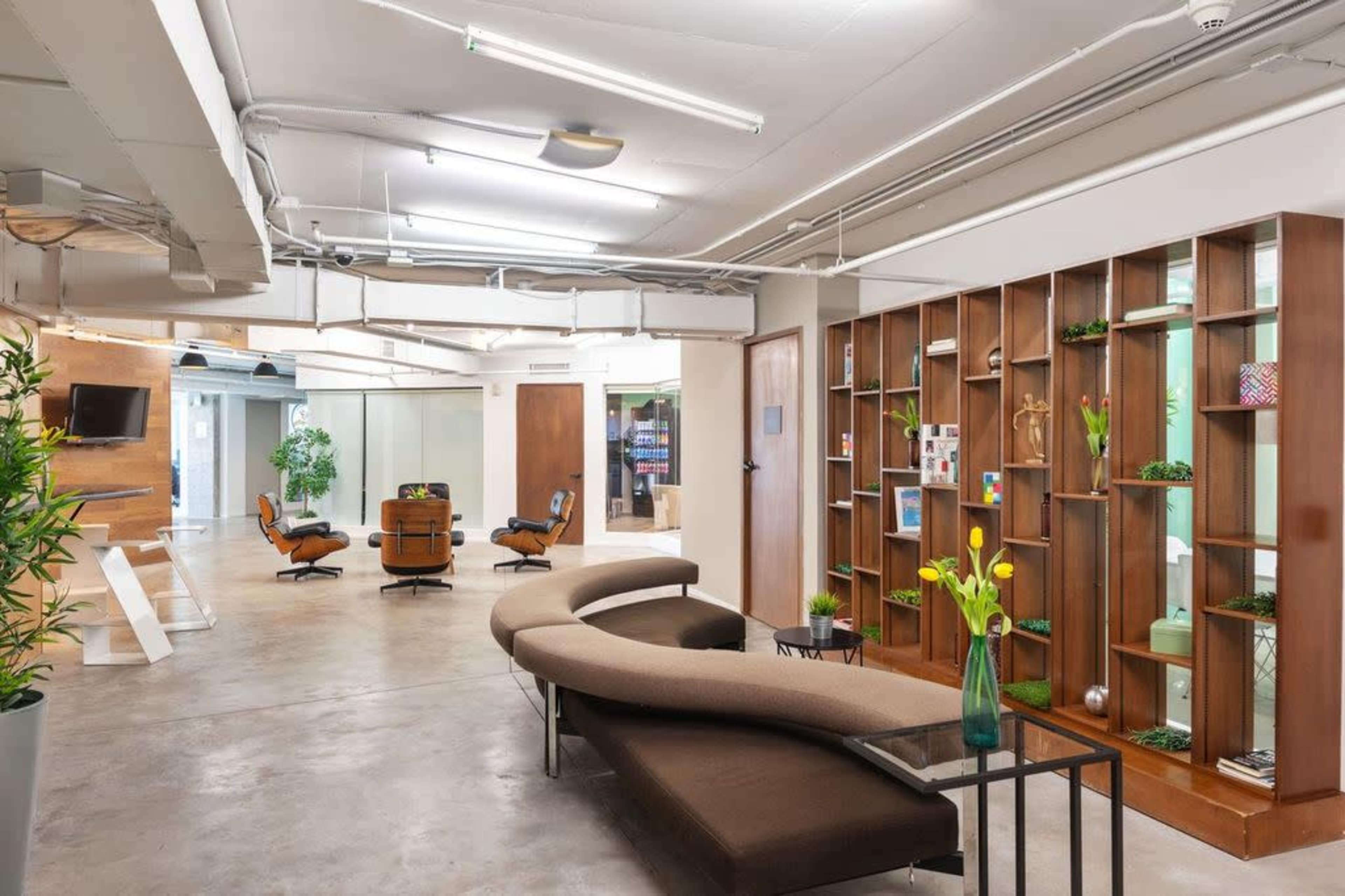 A modern office space with a curved sofa, a coffee table, and wooden shelves displaying decorative items.