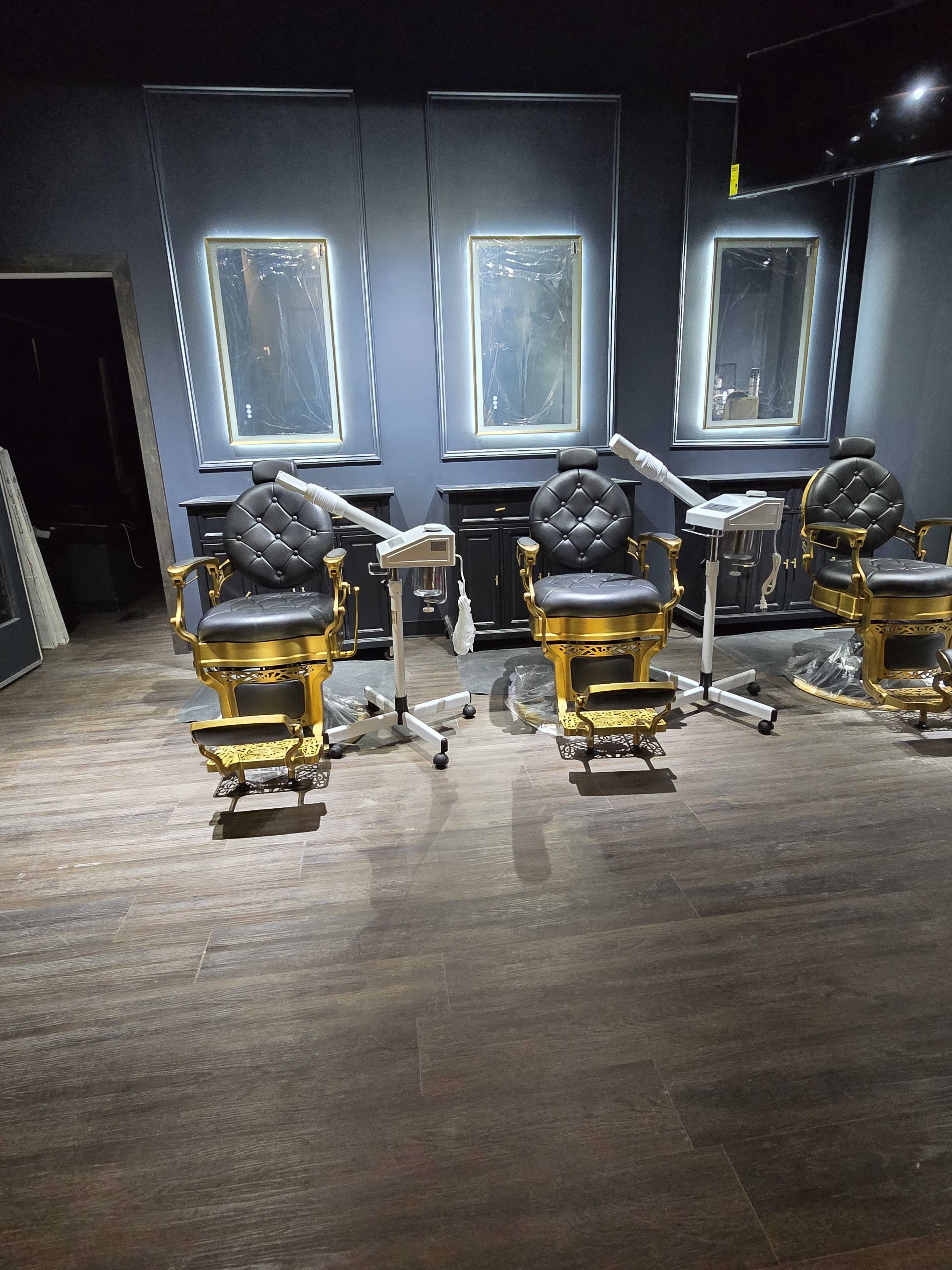 The image shows a dimly lit room with three ornate black and gold barber chairs positioned in front of mirrors.