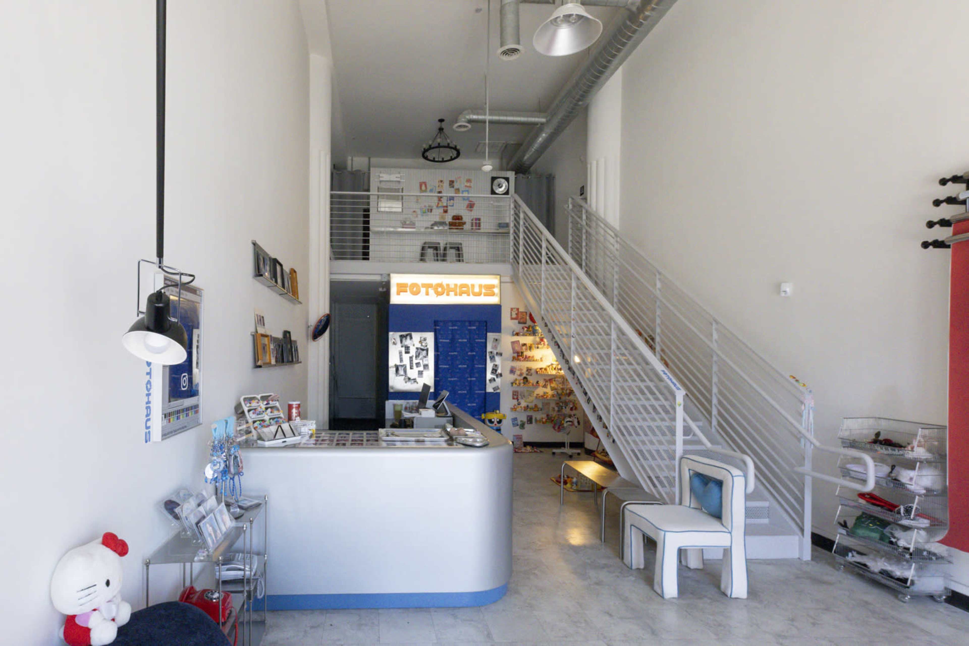 The image shows a modern interior of a photography studio with a reception area, a staircase, and various decorative items on the walls.