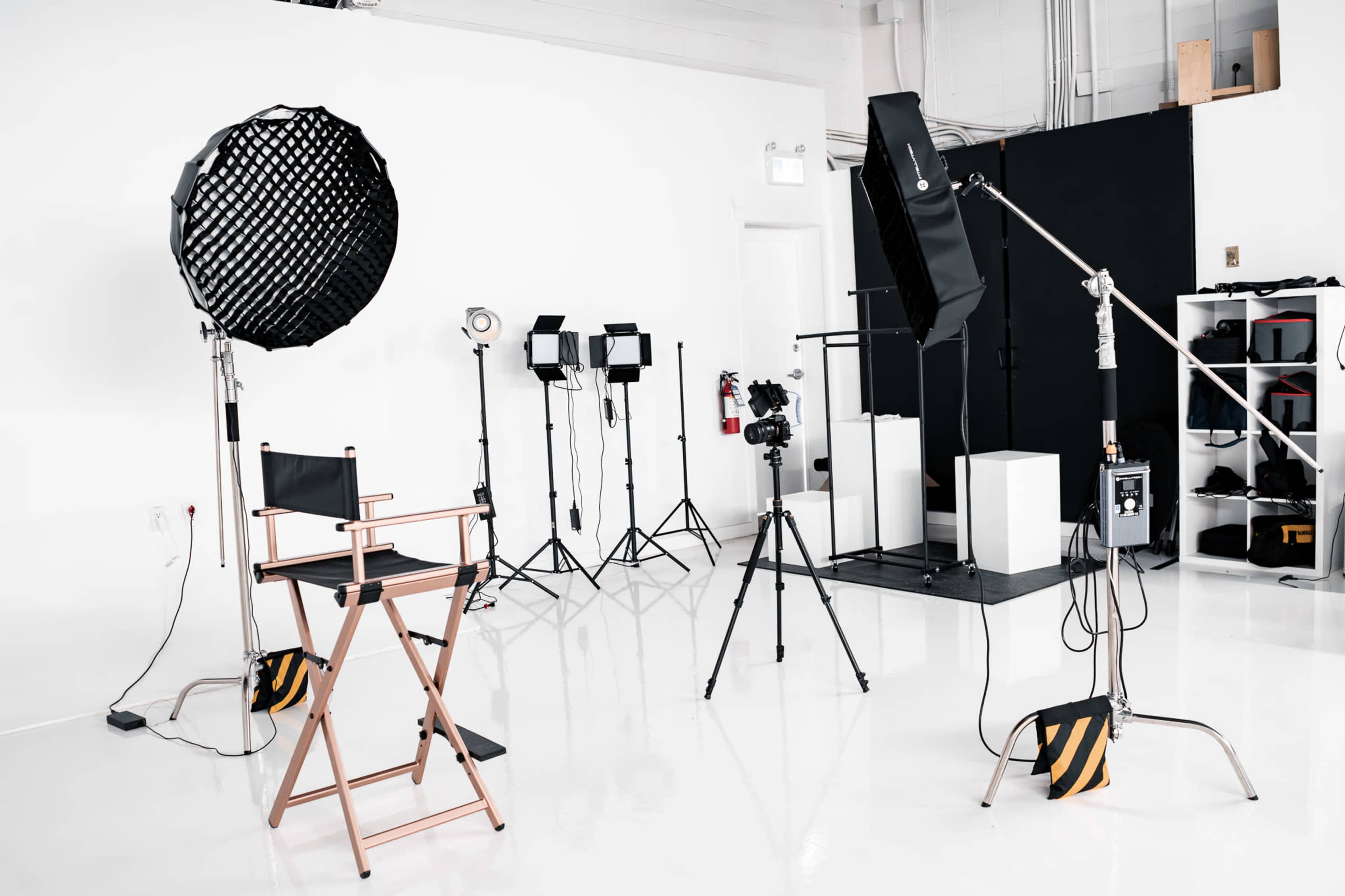 The image shows a photography studio equipped with lighting equipment, a camera on a tripod, and a director's chair.