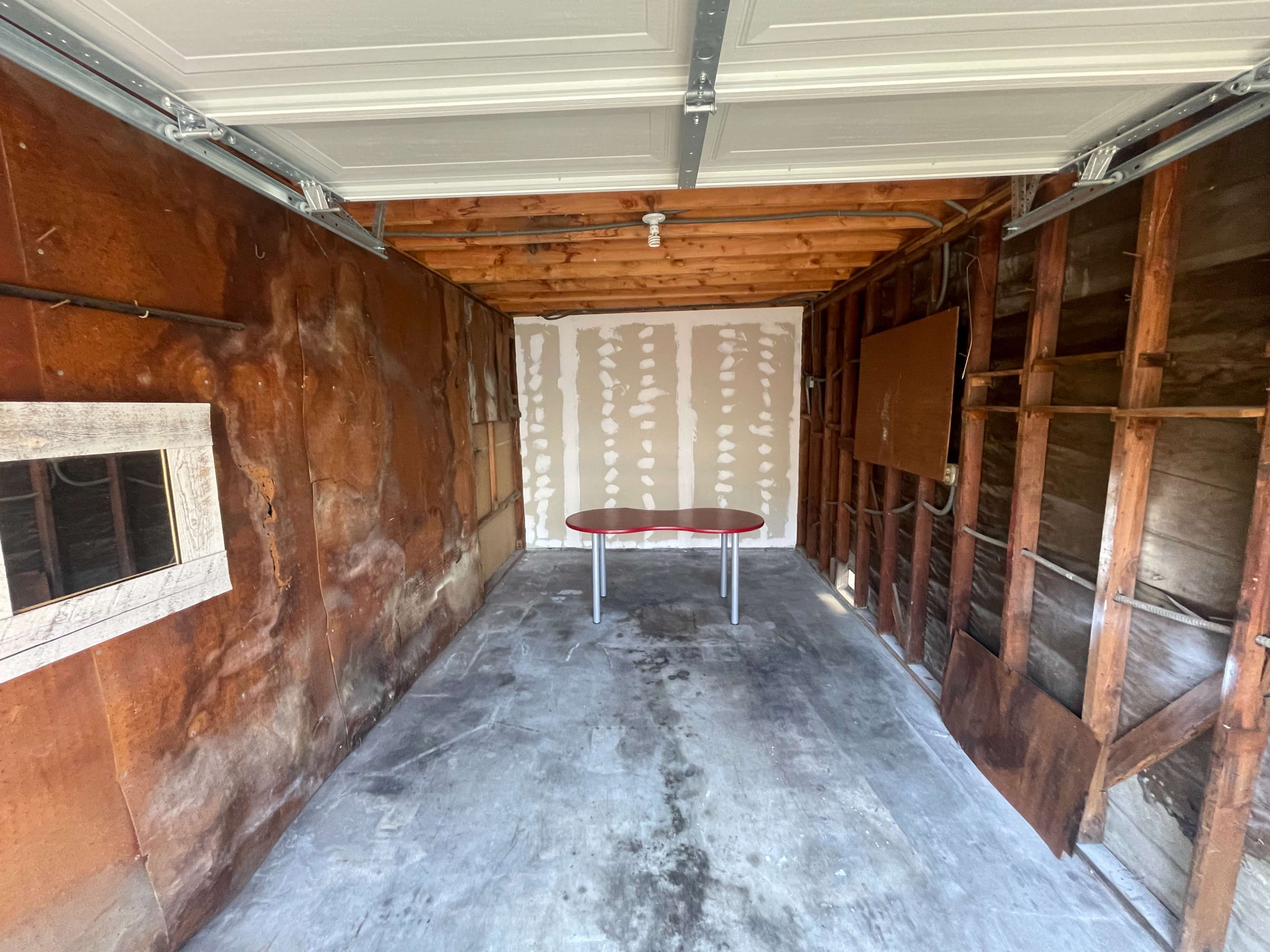 An empty garage with exposed walls, a concrete floor, and a small table in the center.